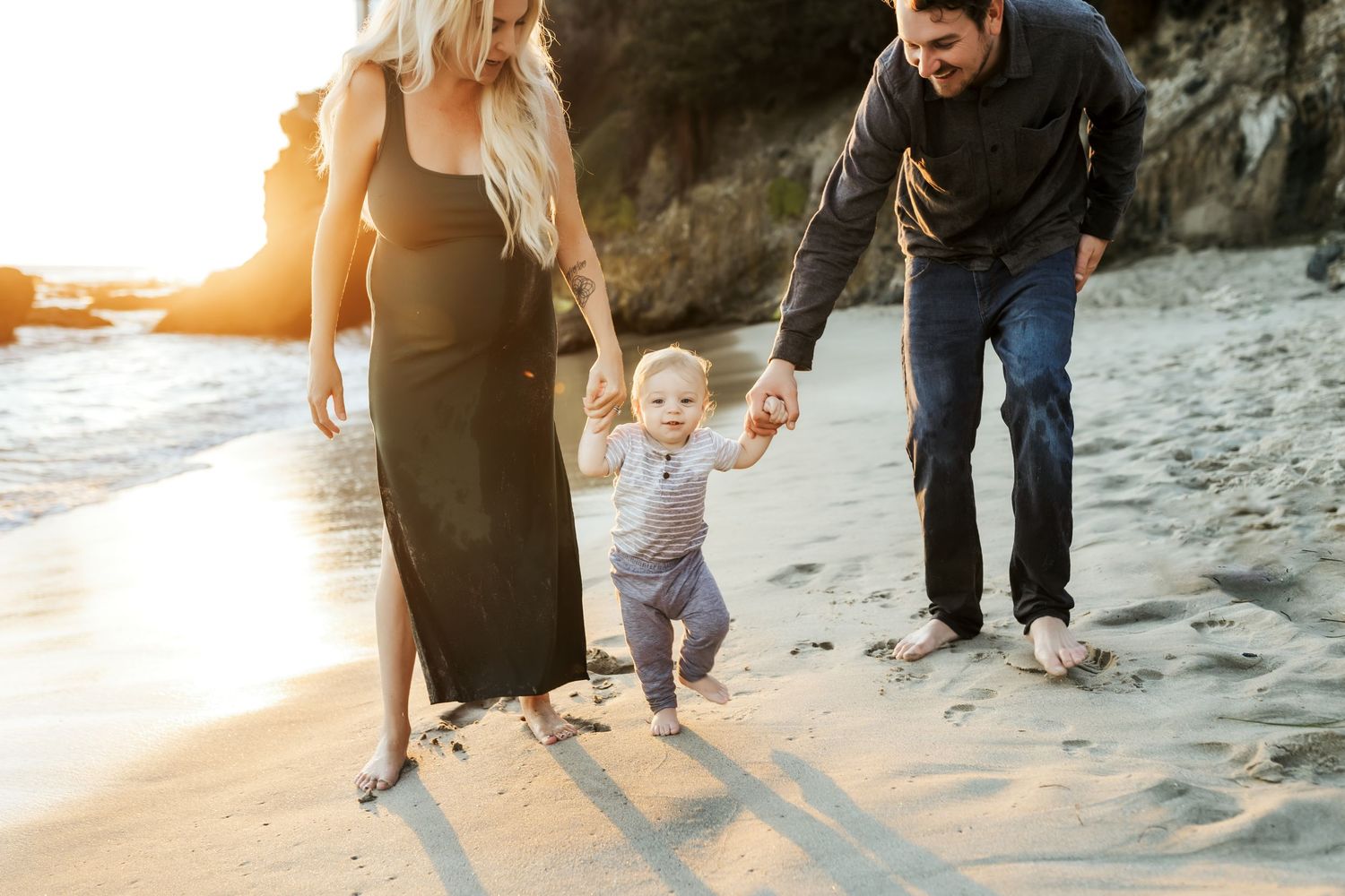 Mother and Father holding toddler's hands while walking on the Beach in Laguna during a relaxed sunset family photo session