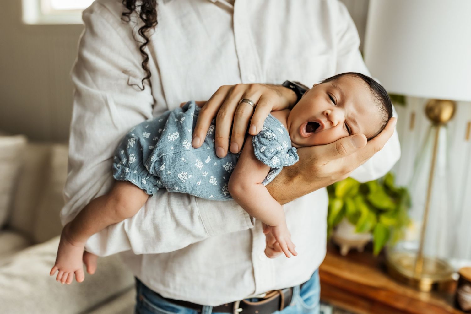 Father holding newborn daughter in his arms at a relaxed at home newborn photo session in Orange County