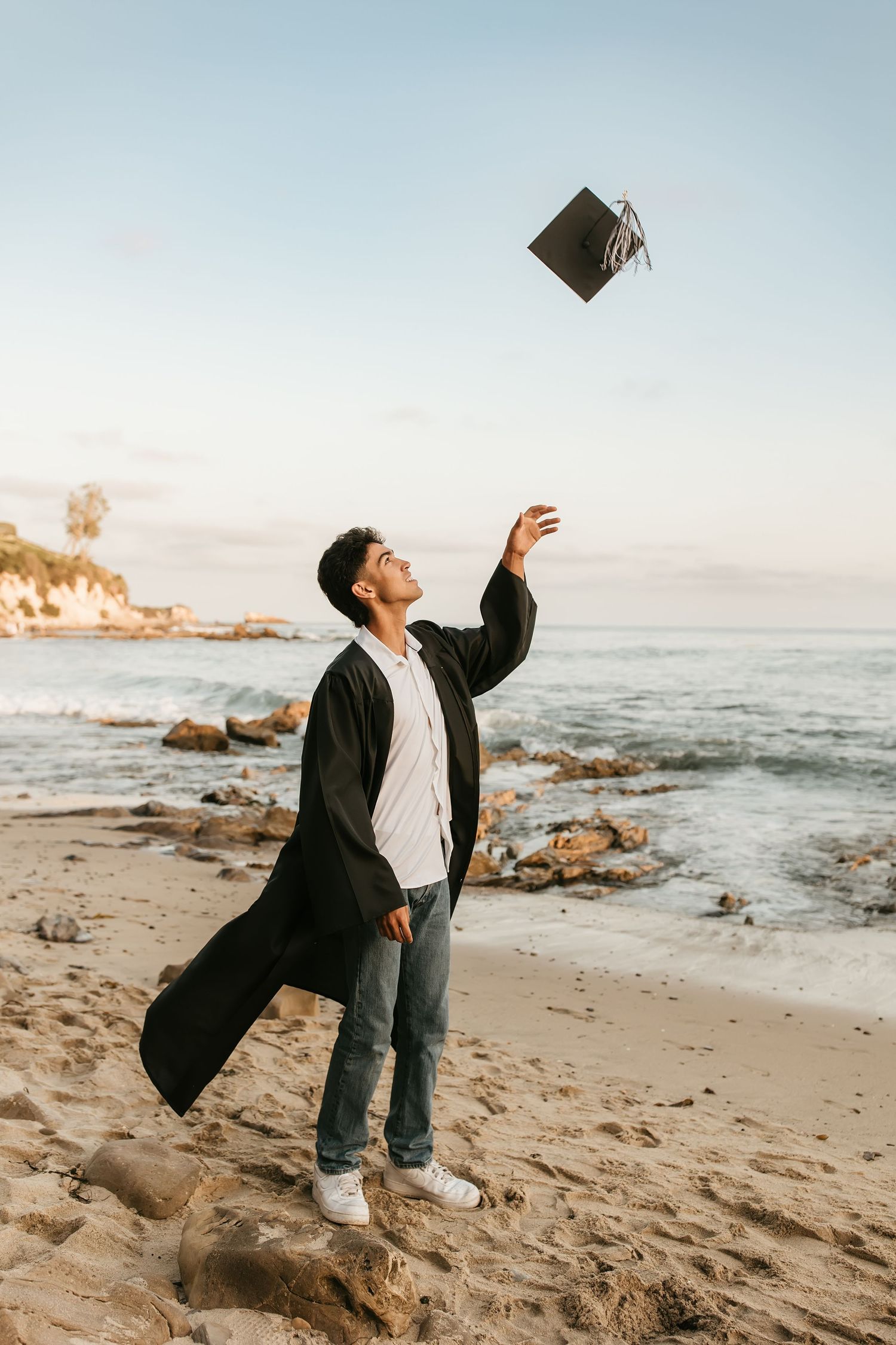 a confident grad throwing his cap in the air at the beach in Laguna Beach, CA