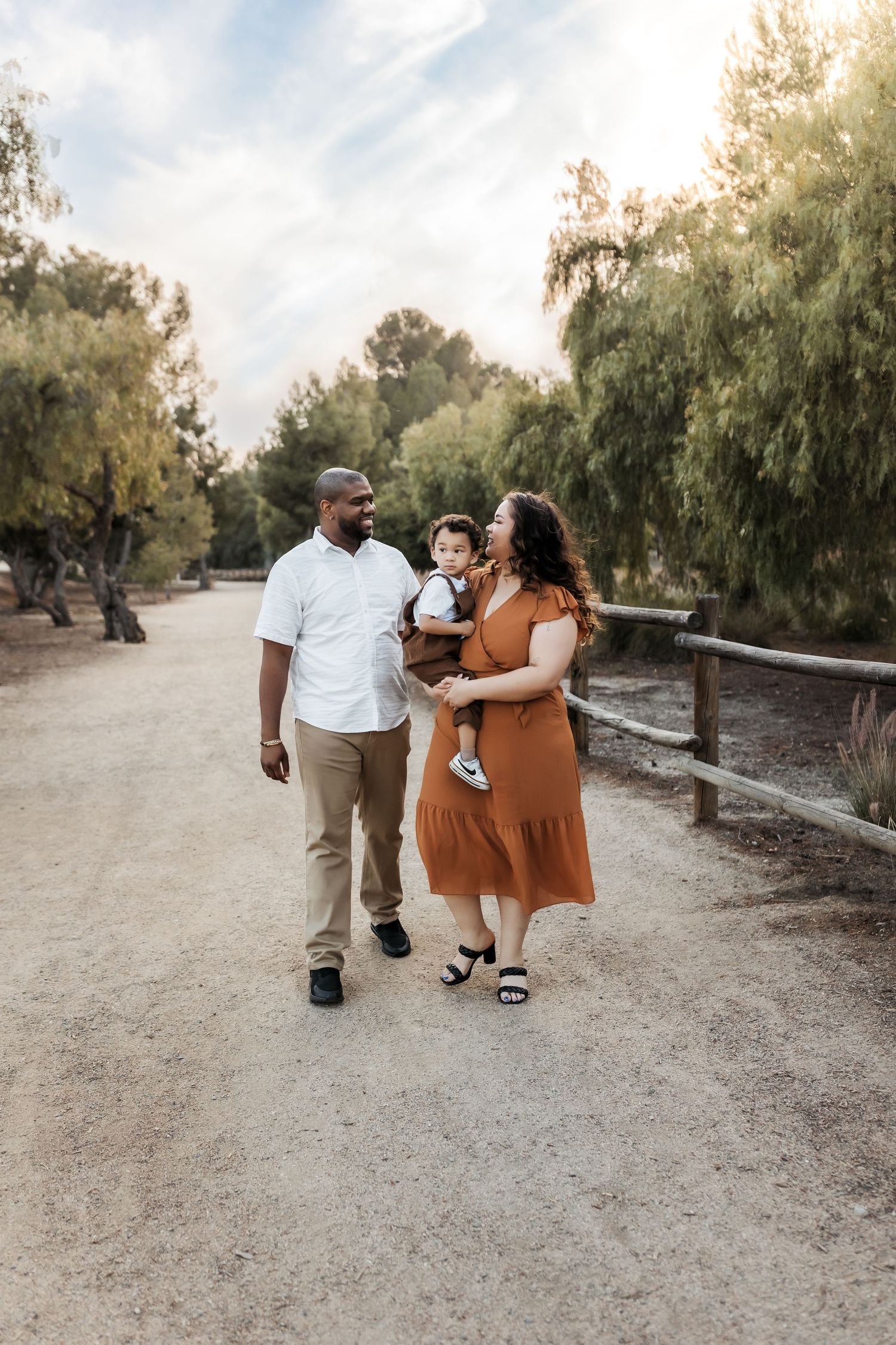 A mom and dad holding their toddler walking and looking at each other during a family portrait session in Orange County