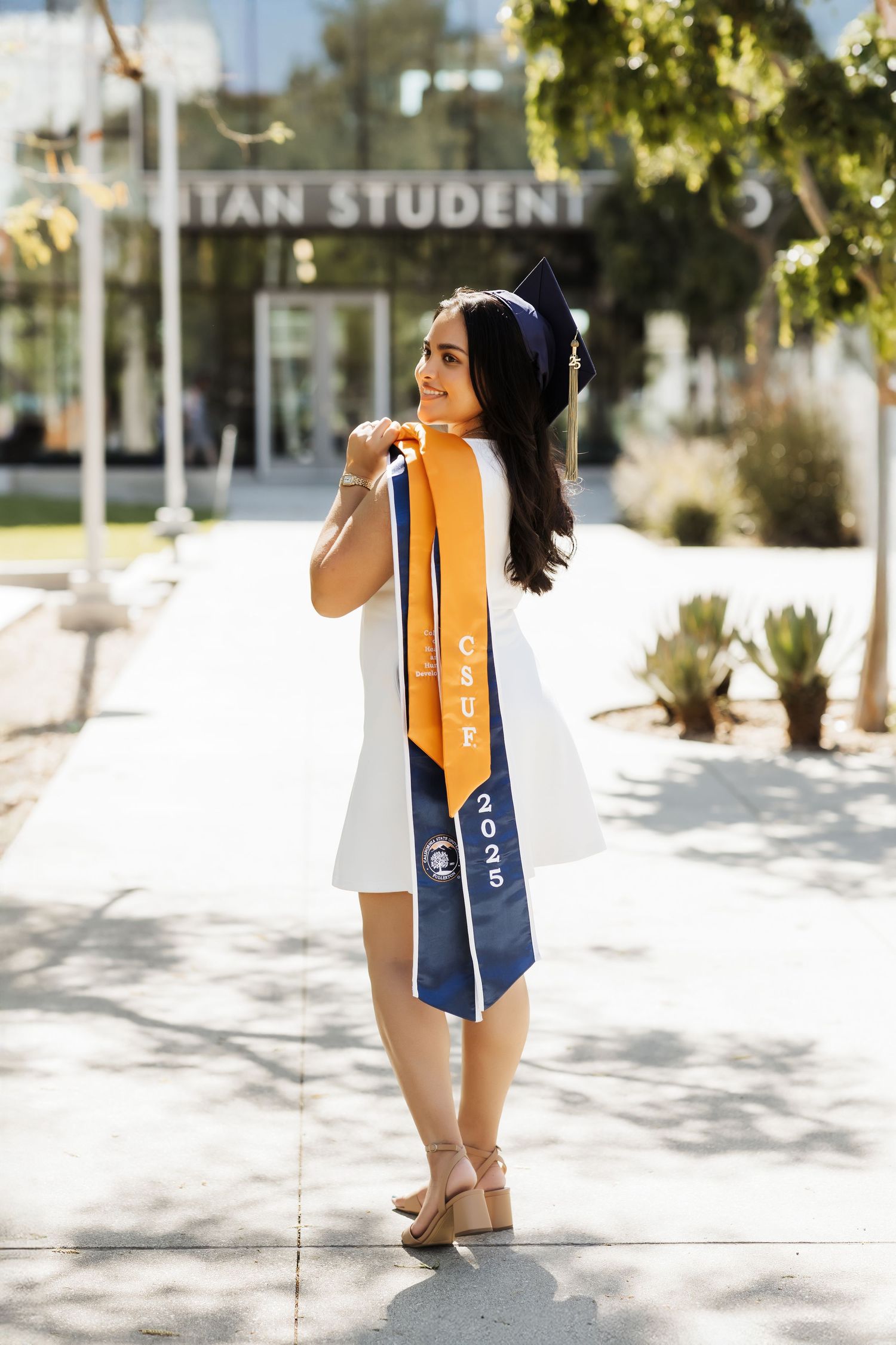 CSUF graduate in cap and sashes during outdoor grad photos.