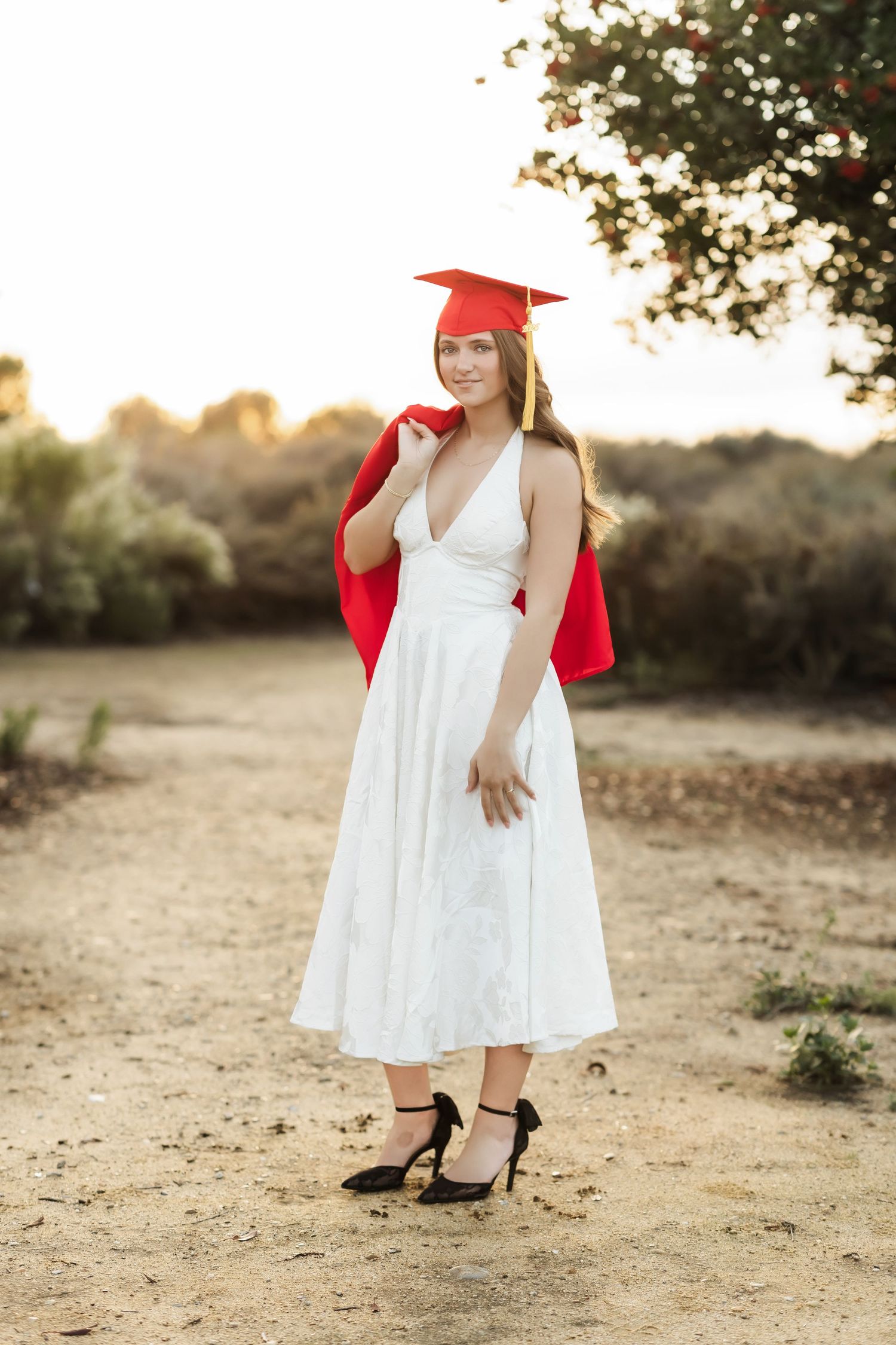 Senior girl in white dress and cap and gown during a sunset session in Fullerton, CA