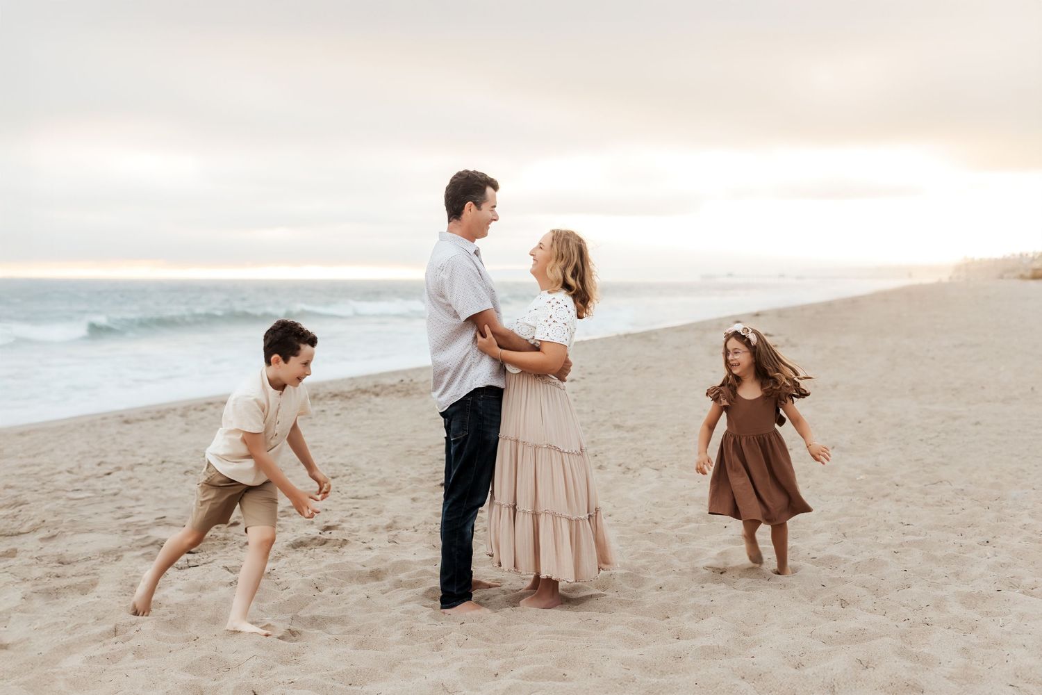 A mom and dad looking at each other while the kids run around them during a relaxed family photo session on the beach in Orange County