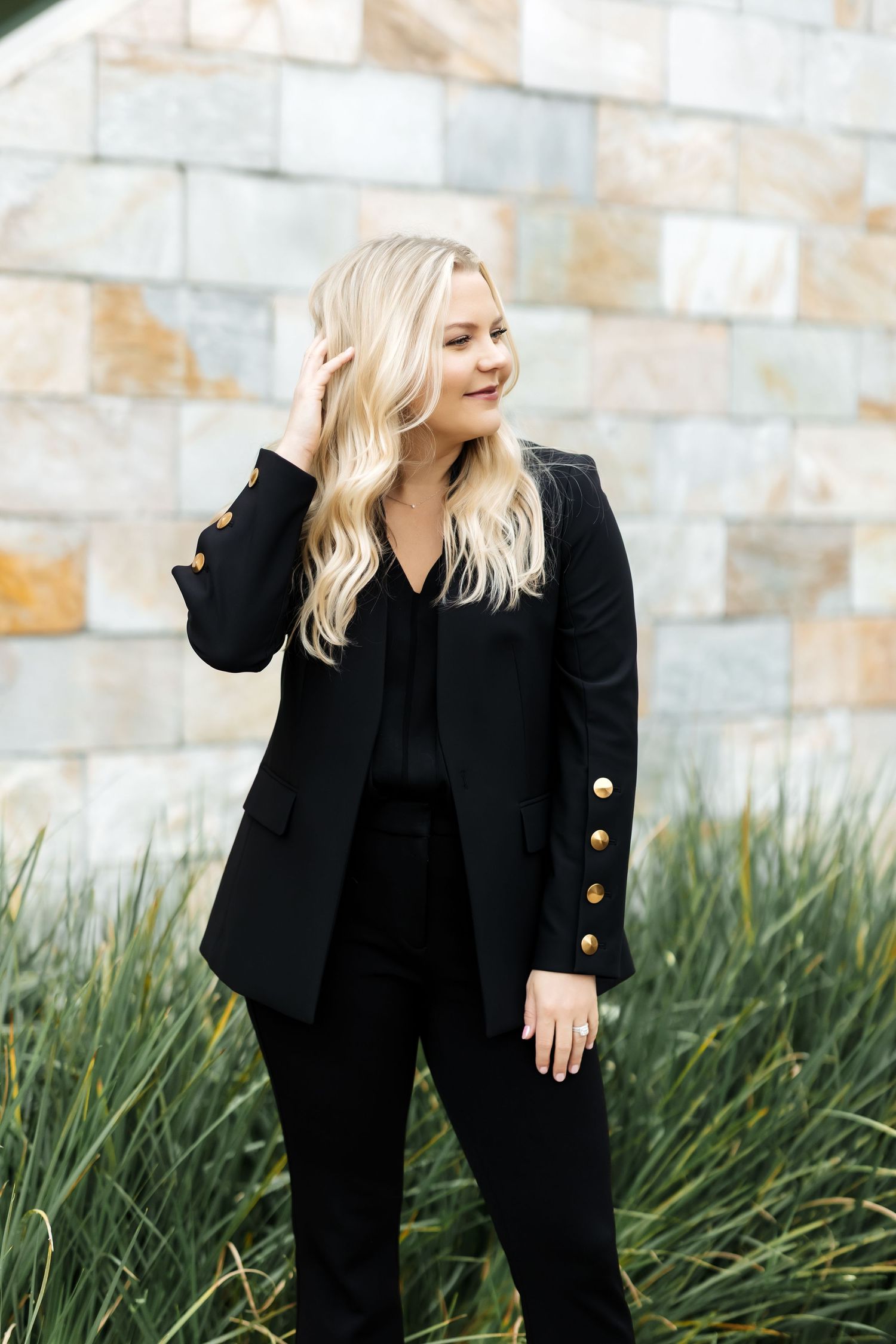 Modern headshot of woman in a black suite with her hand in her hair