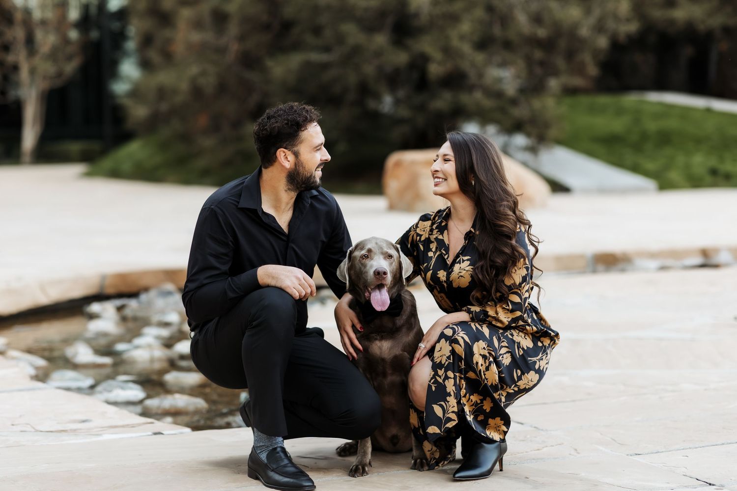 Couple kneeling and smiling at each other while their dog looks at the camera during a session in Orange County