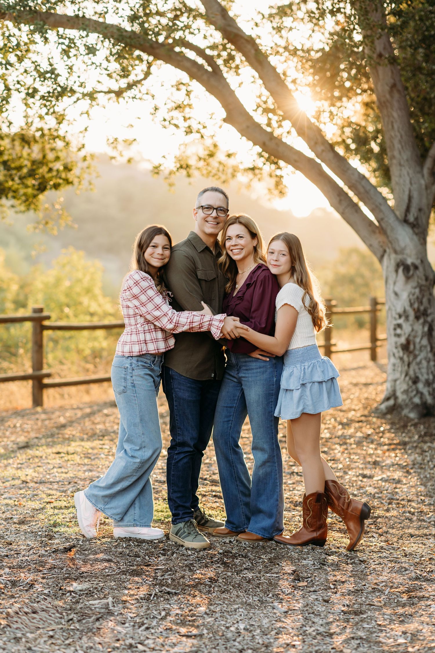 A family wrapping their arms around each other during a family photo session while sunlight peaks through a tree behind them in Brea, CA