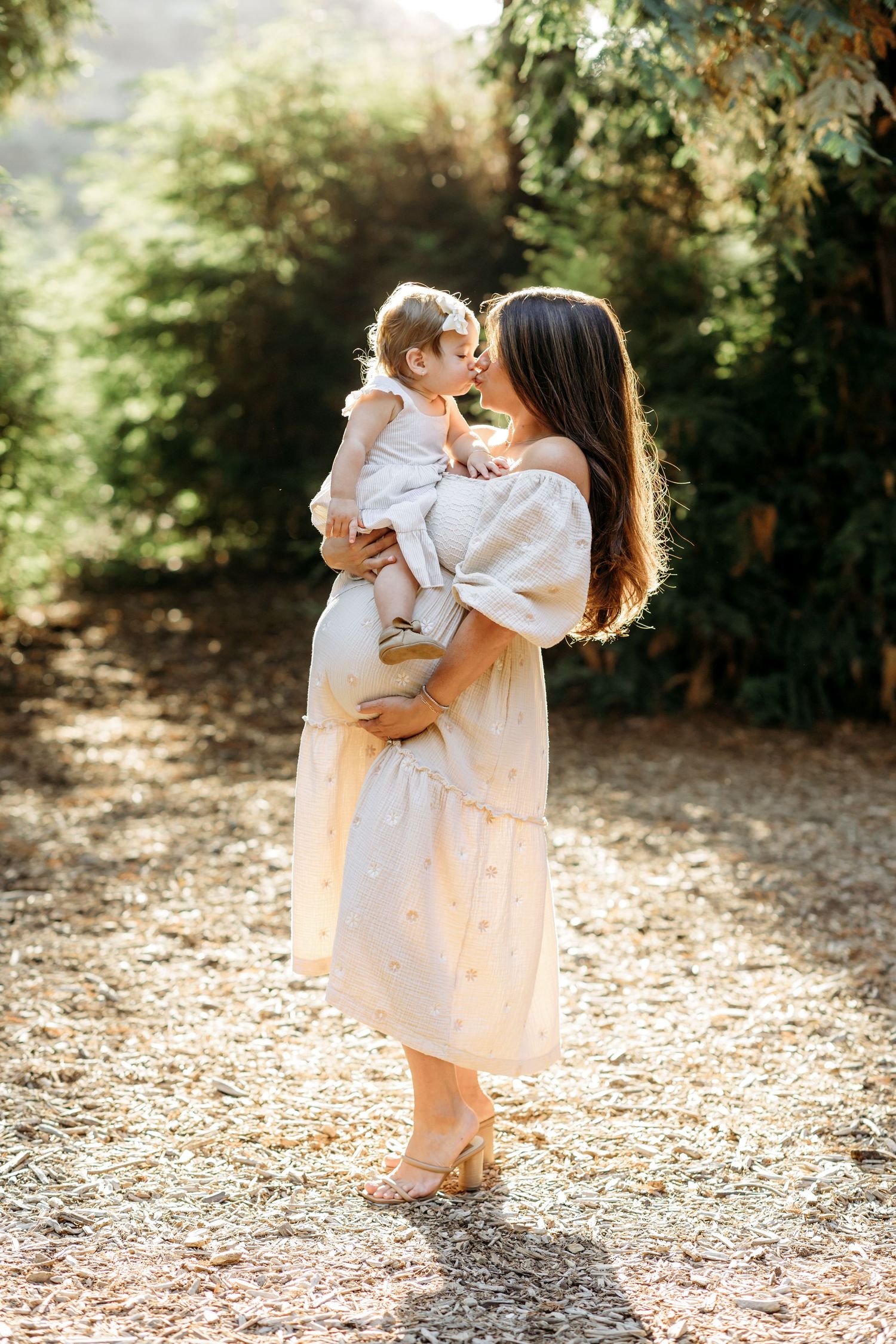 Mom hold her baby girl while placing her hand on her belly during a maternity portrait session in Brea, CA