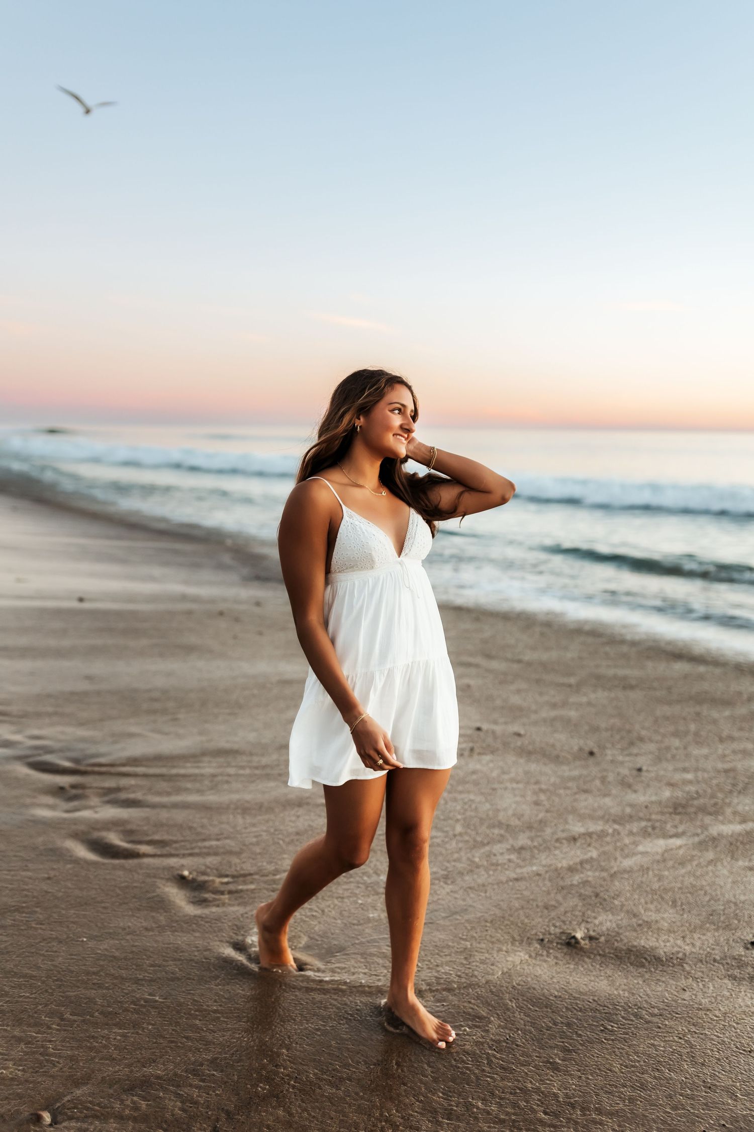 Senior portrait of girl walking along the beach in a white dress
