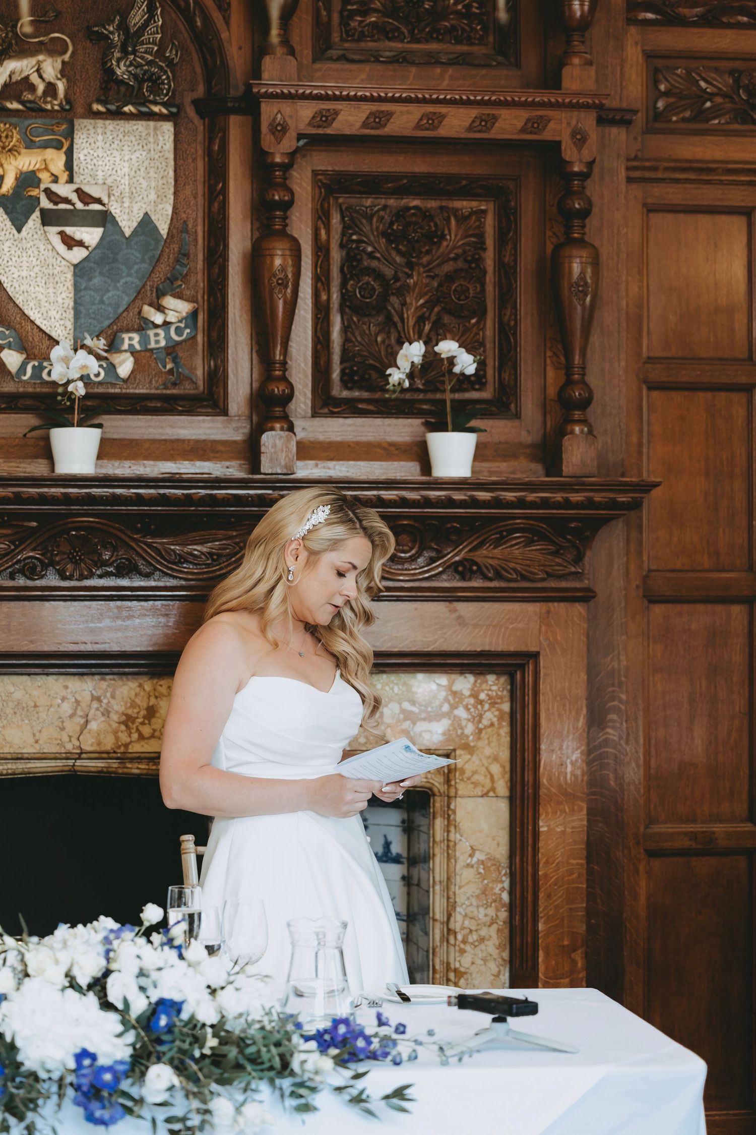 Bride reading speech at reception with white and blue floral decorations.
