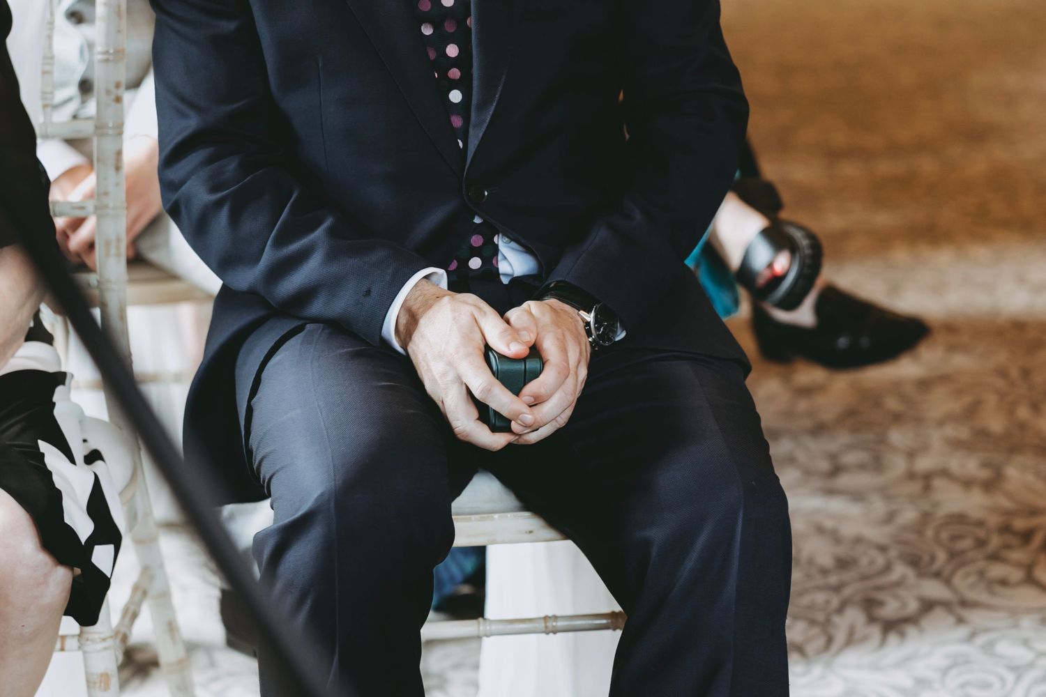 Groomsmen in black suits sit in a row during a formal wedding ceremony.