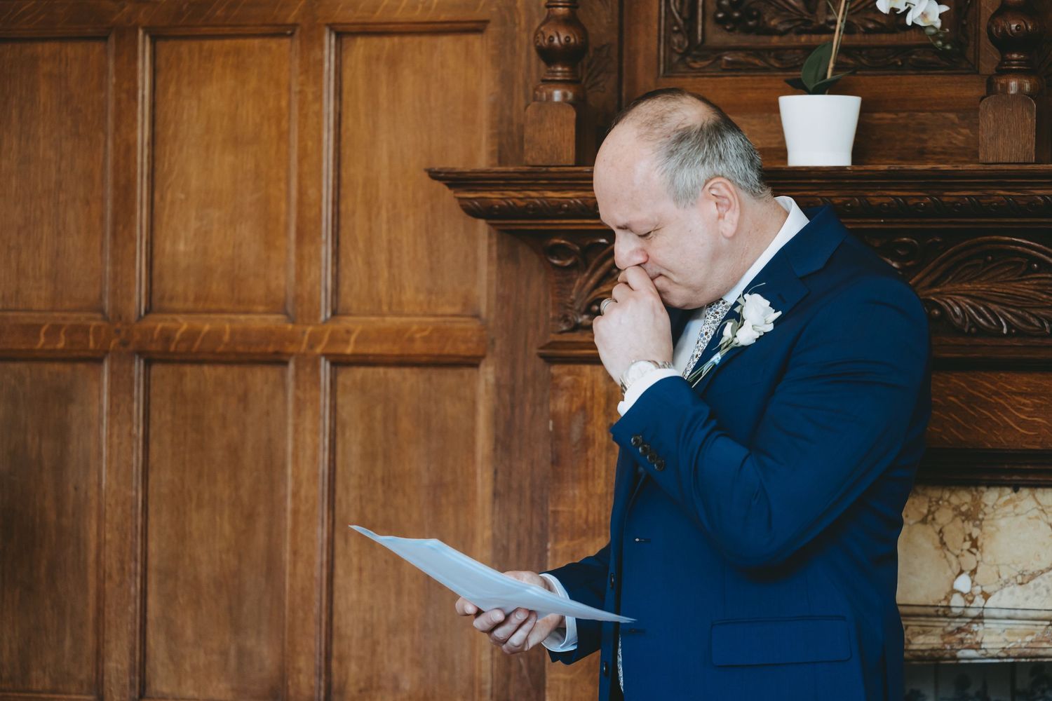 Speaker reviews notes thoughtfully during formal event in wood-paneled room.