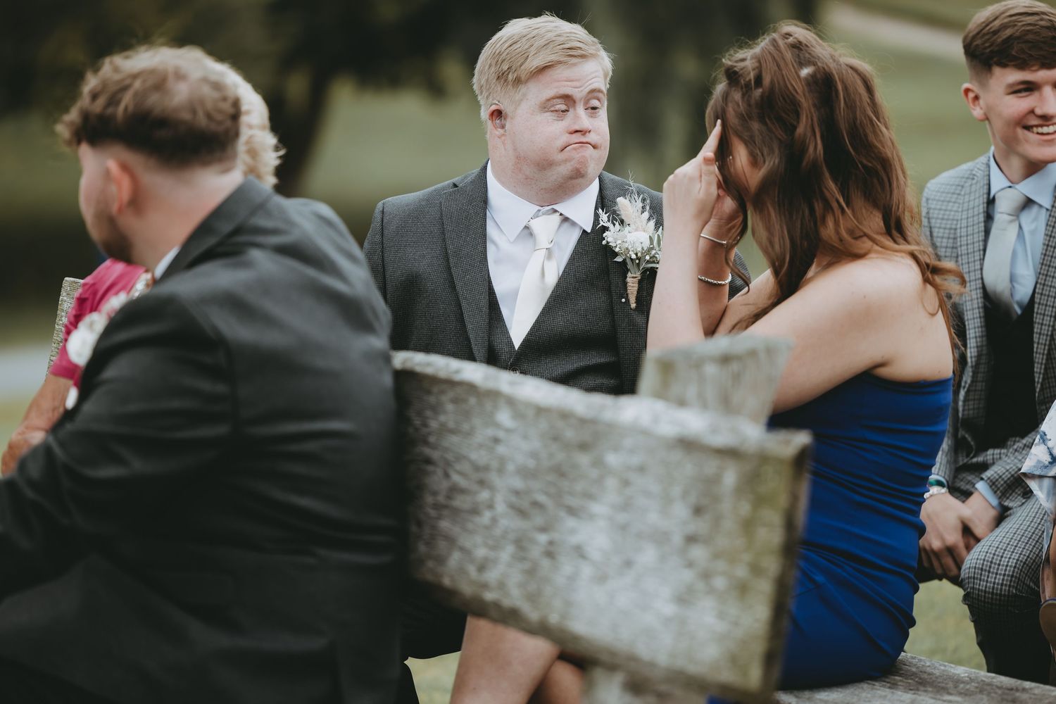 Wedding attendees sitting on rustic benches during a garden ceremony.