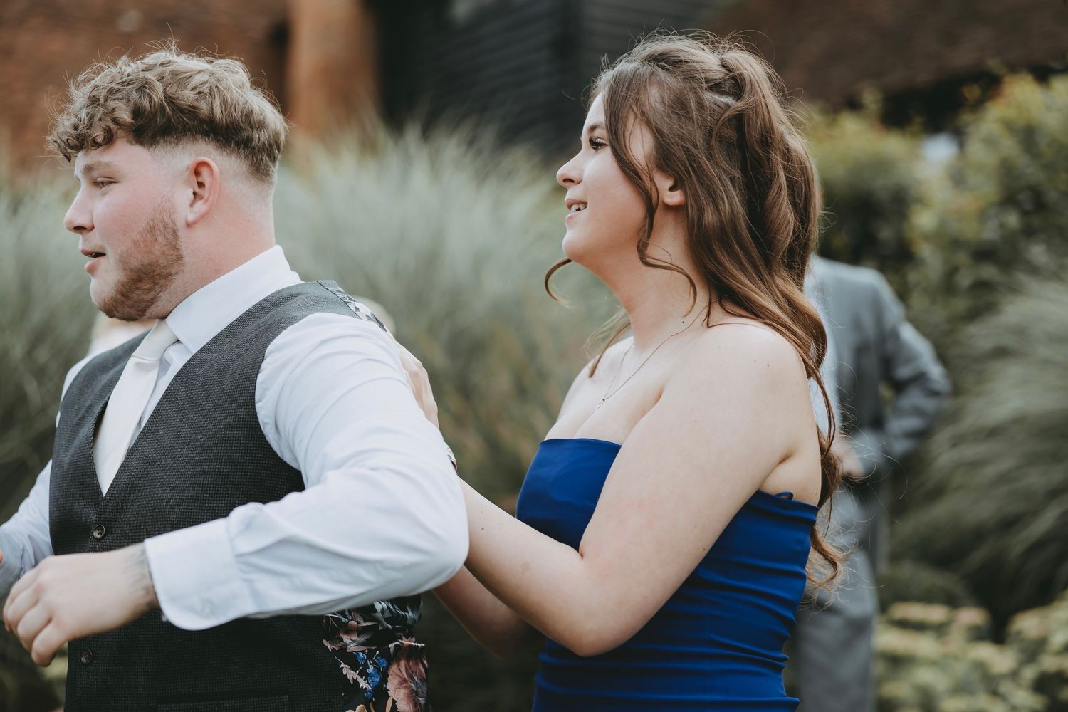 Wedding party members in blue and white attire dance joyfully outdoors.