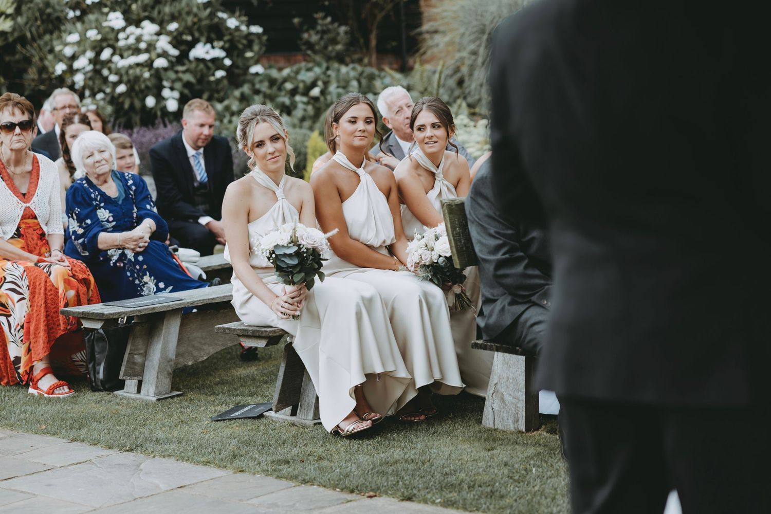 Wedding guests seated outdoors watching ceremony under trees.