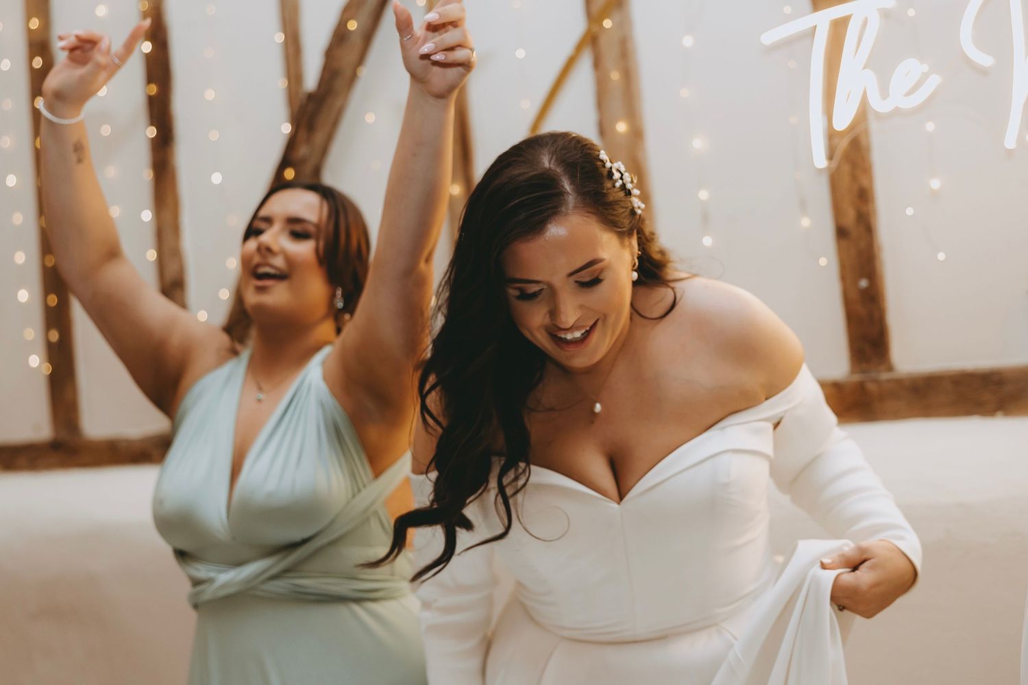 Two people celebrating joyfully with raised arms at a wedding reception with twinkling lights in the background.