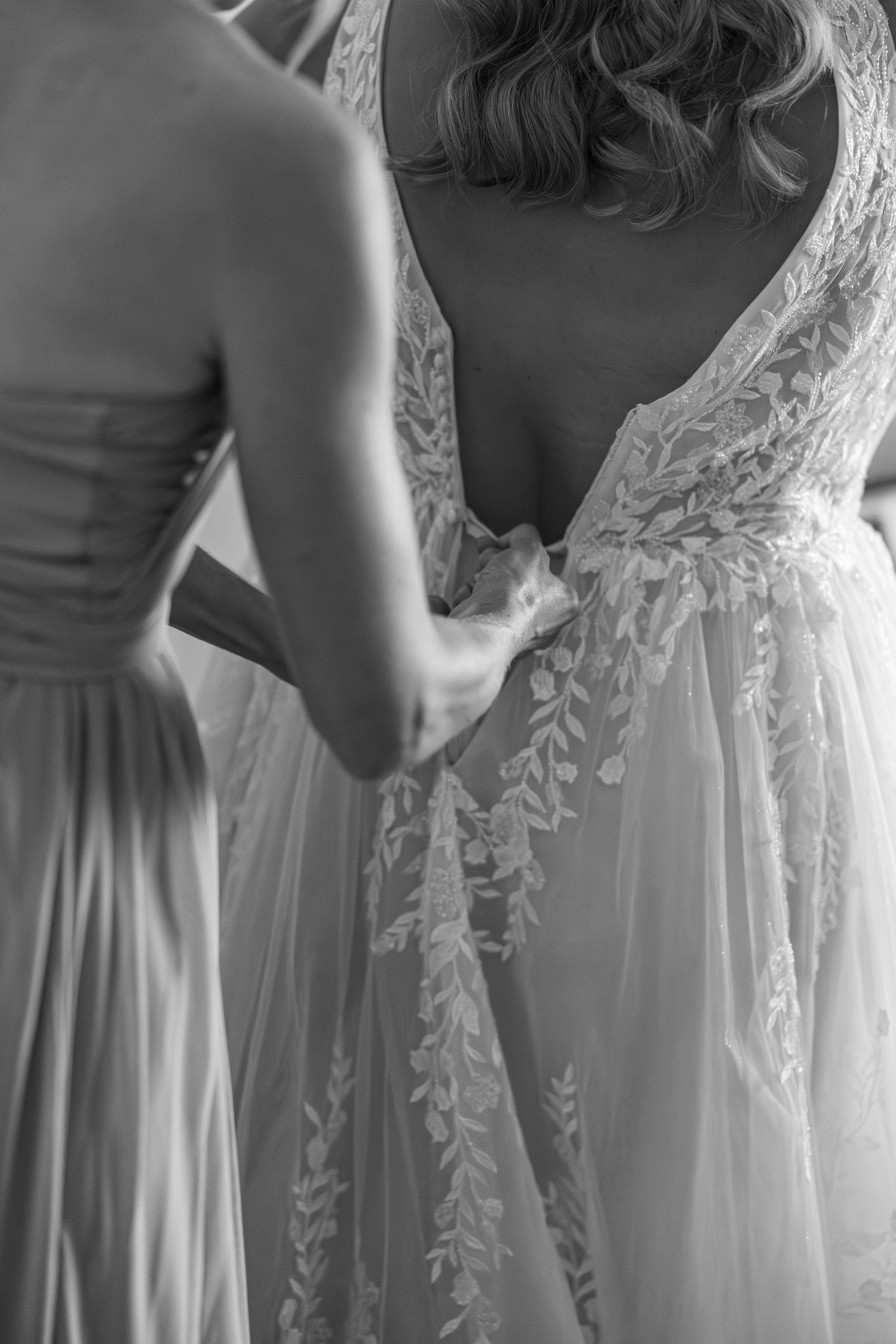 Bridesmaids in pale blue dresses help adjust a white wedding gown with delicate lace details.