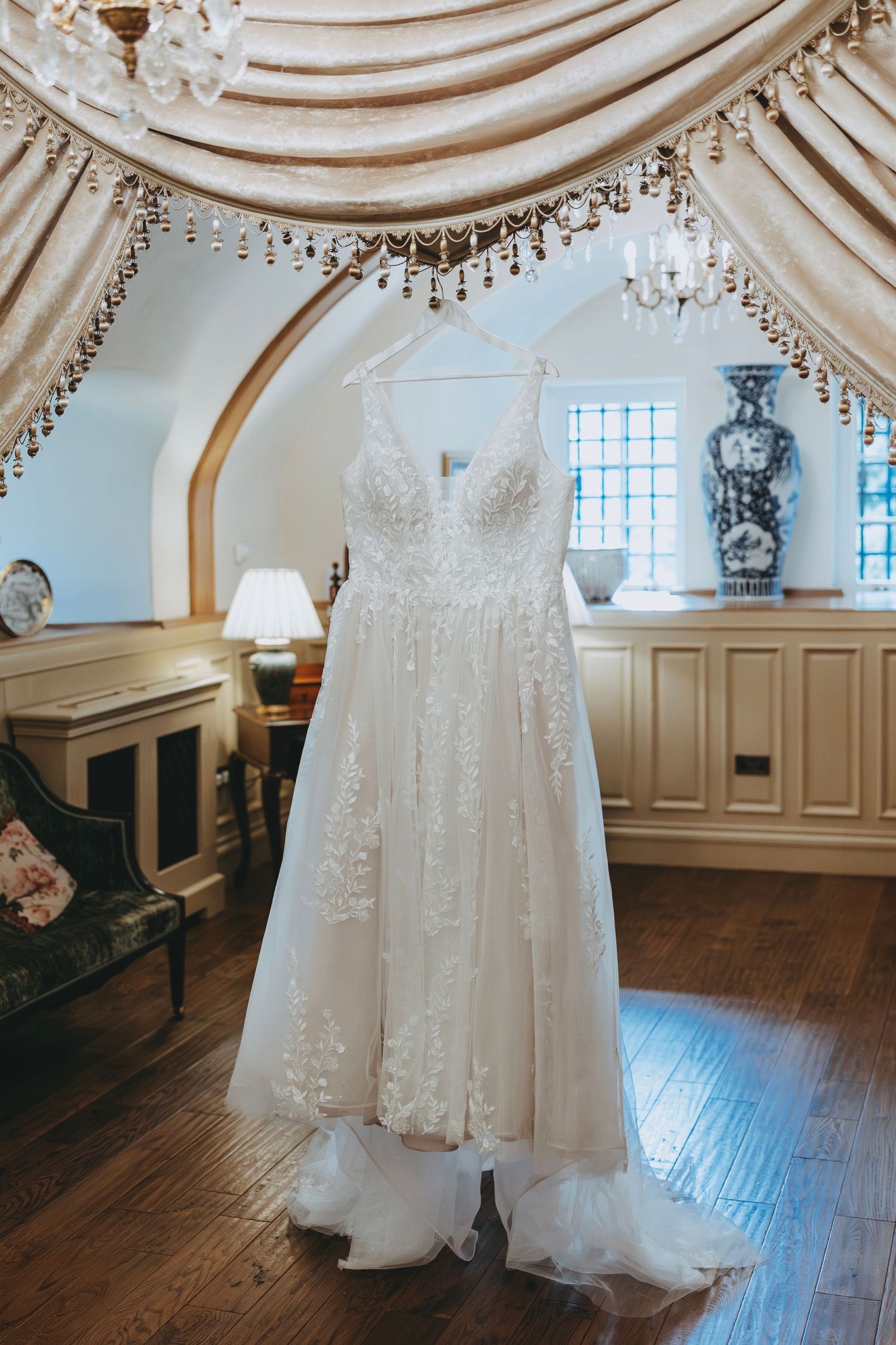 Elegant white wedding dress displayed in a grand room with ornate ceiling and wooden floors.