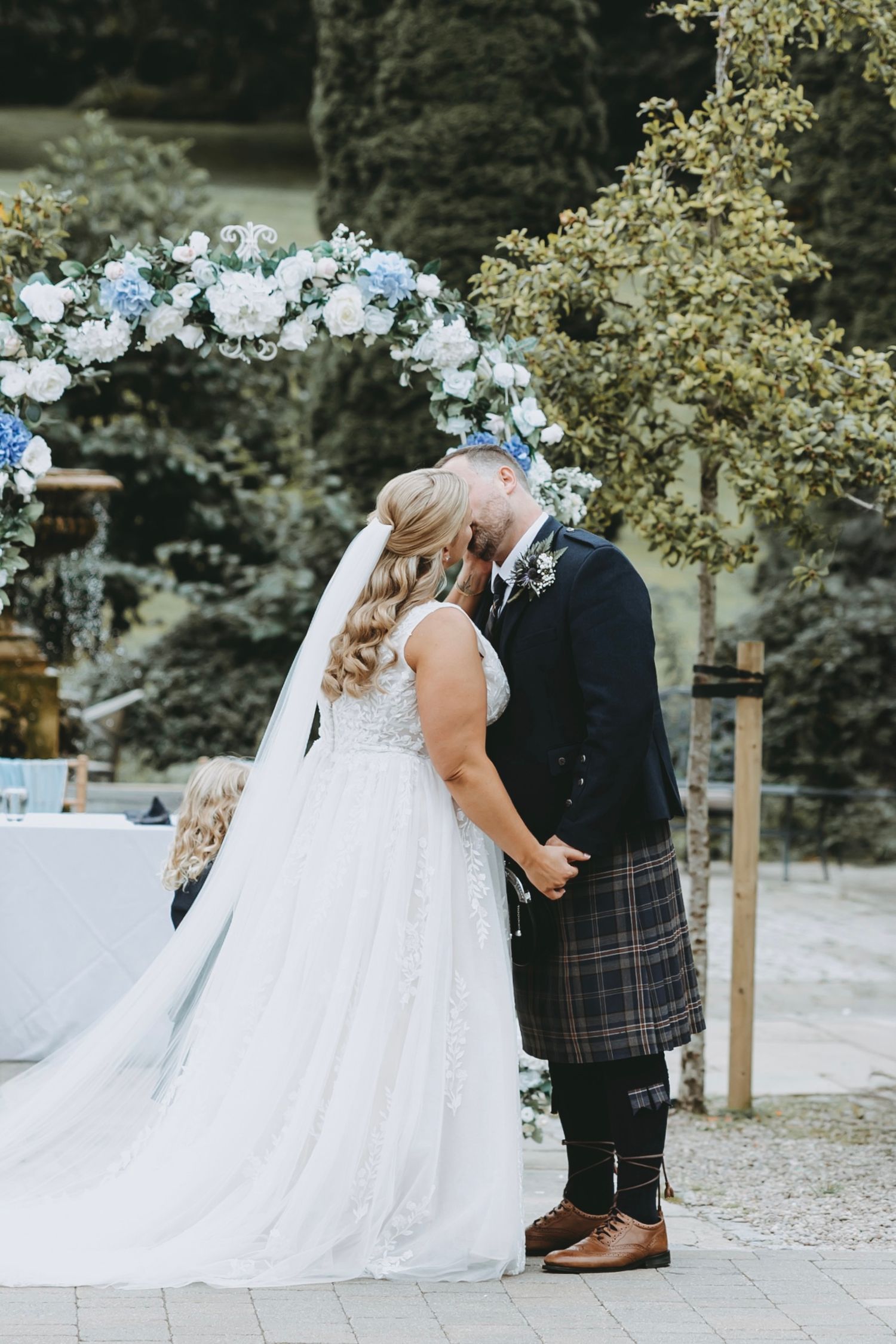 A couple stands at the altar during their outdoor wedding ceremony with guests seated on wooden chairs.