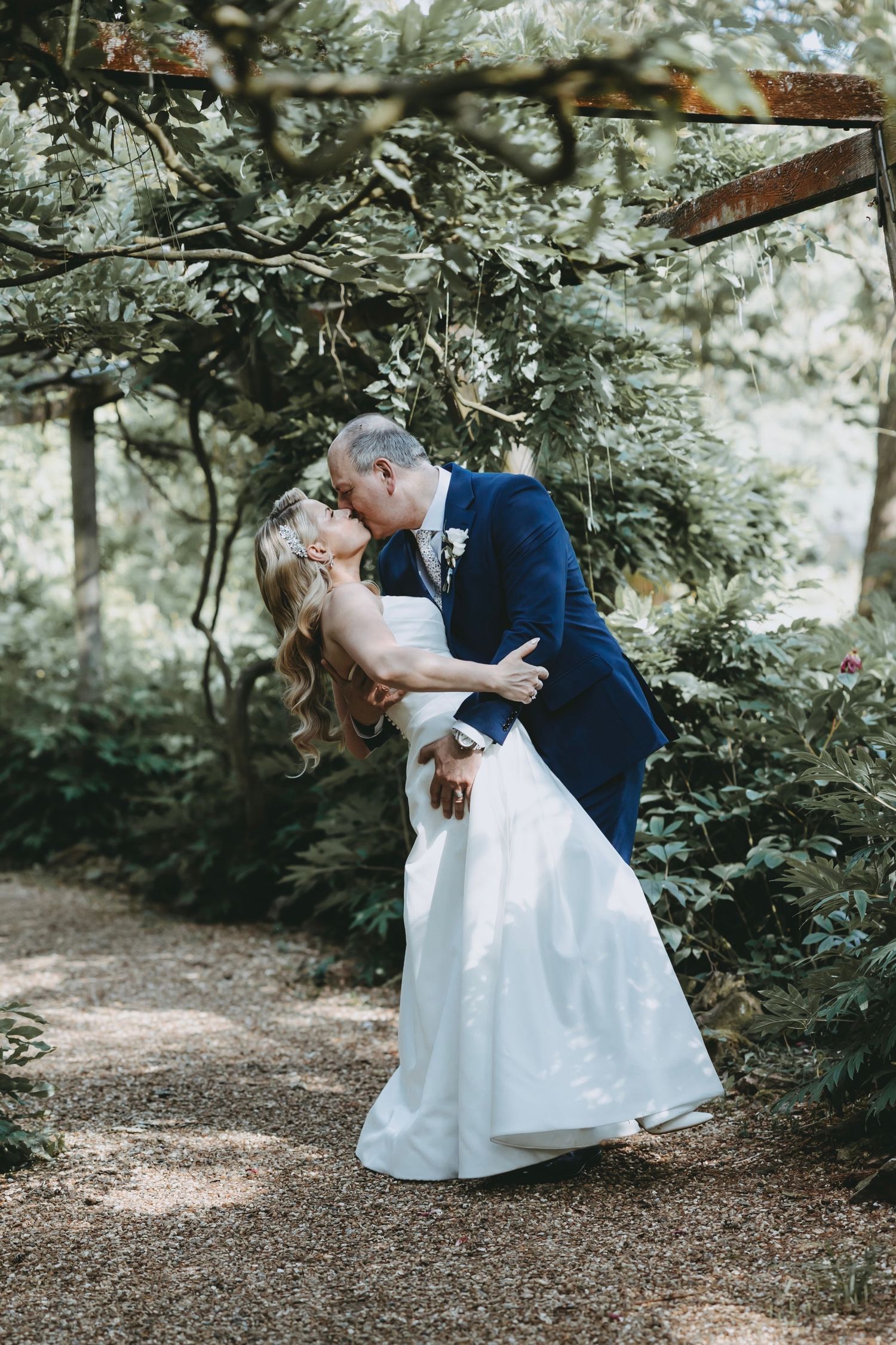 A couple shares a romantic dip kiss under a lush garden arbor during their wedding.