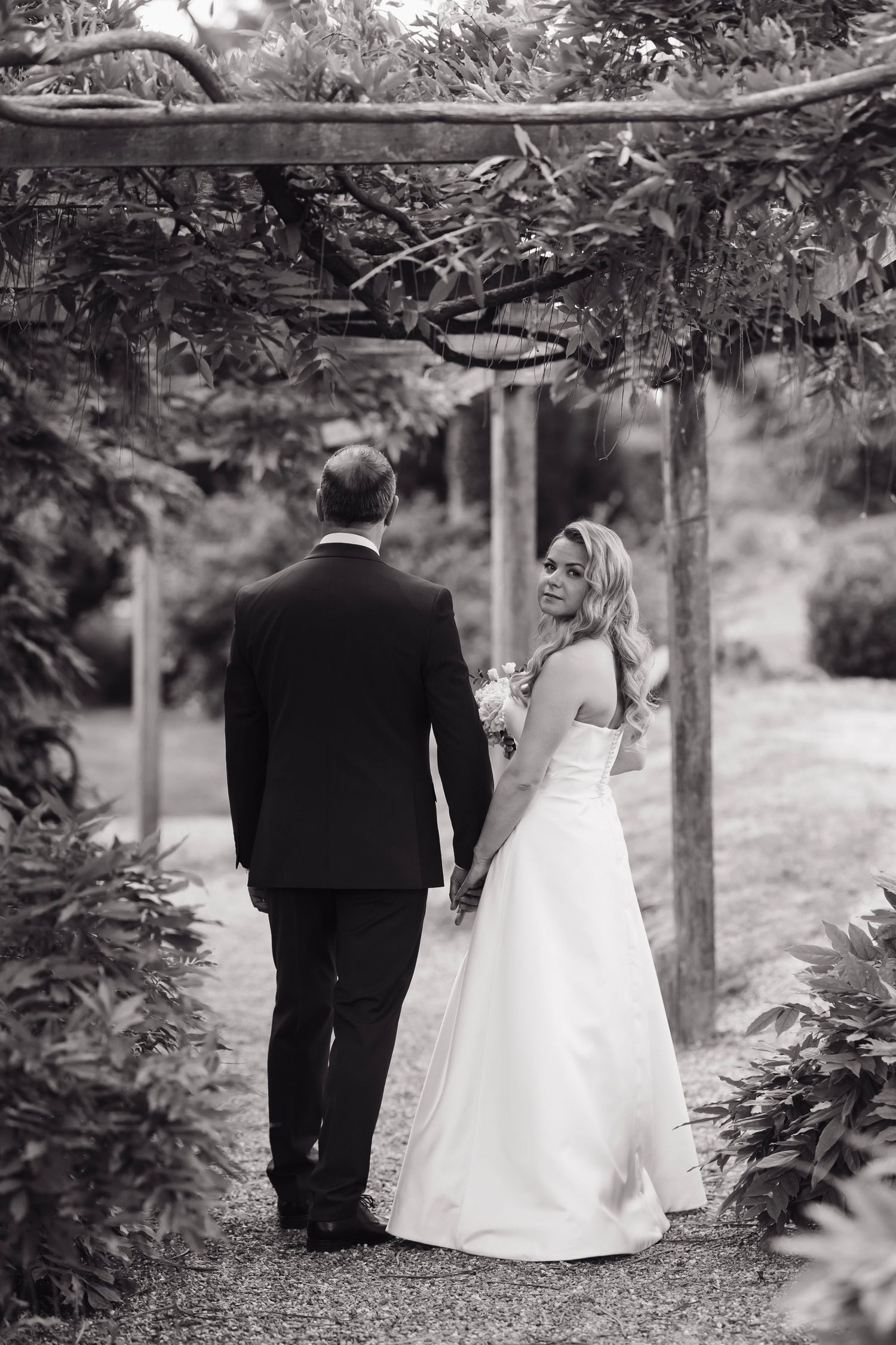 Black and white wedding photo of a couple walking through a garden path.