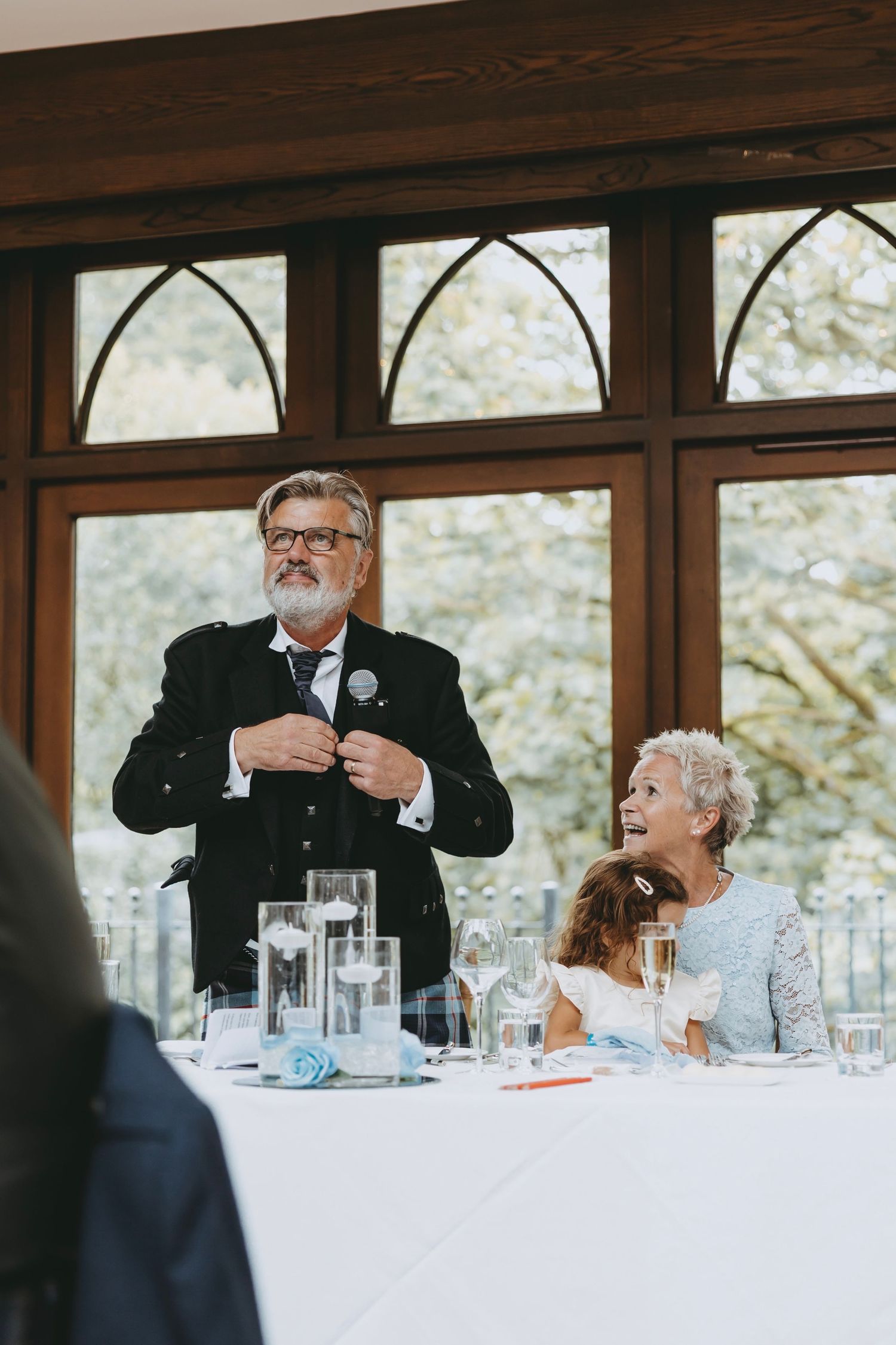 Wedding reception guests listening to speeches at formal dining tables.