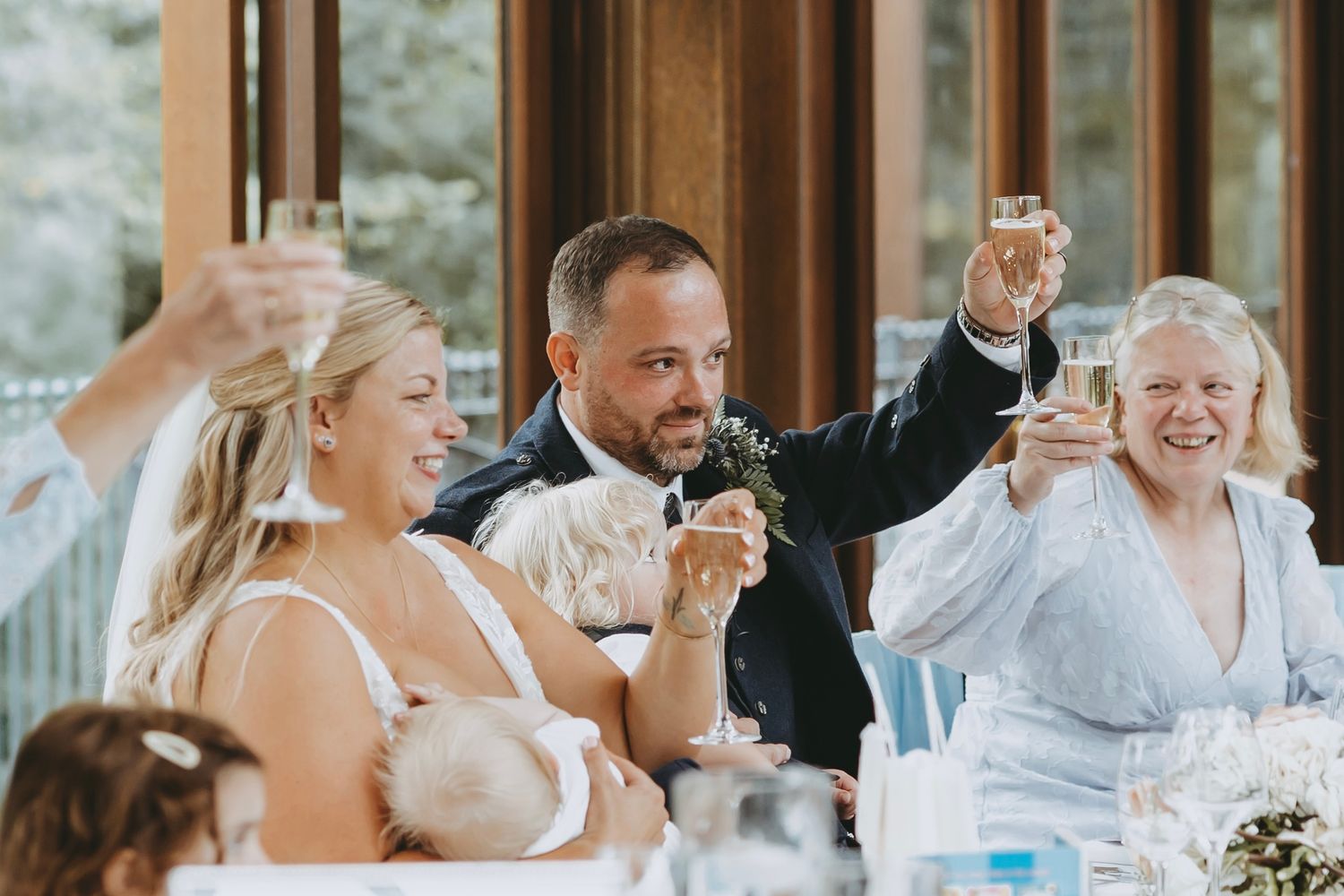 Natural light illuminates wedding reception guests enjoying dinner conversation.
