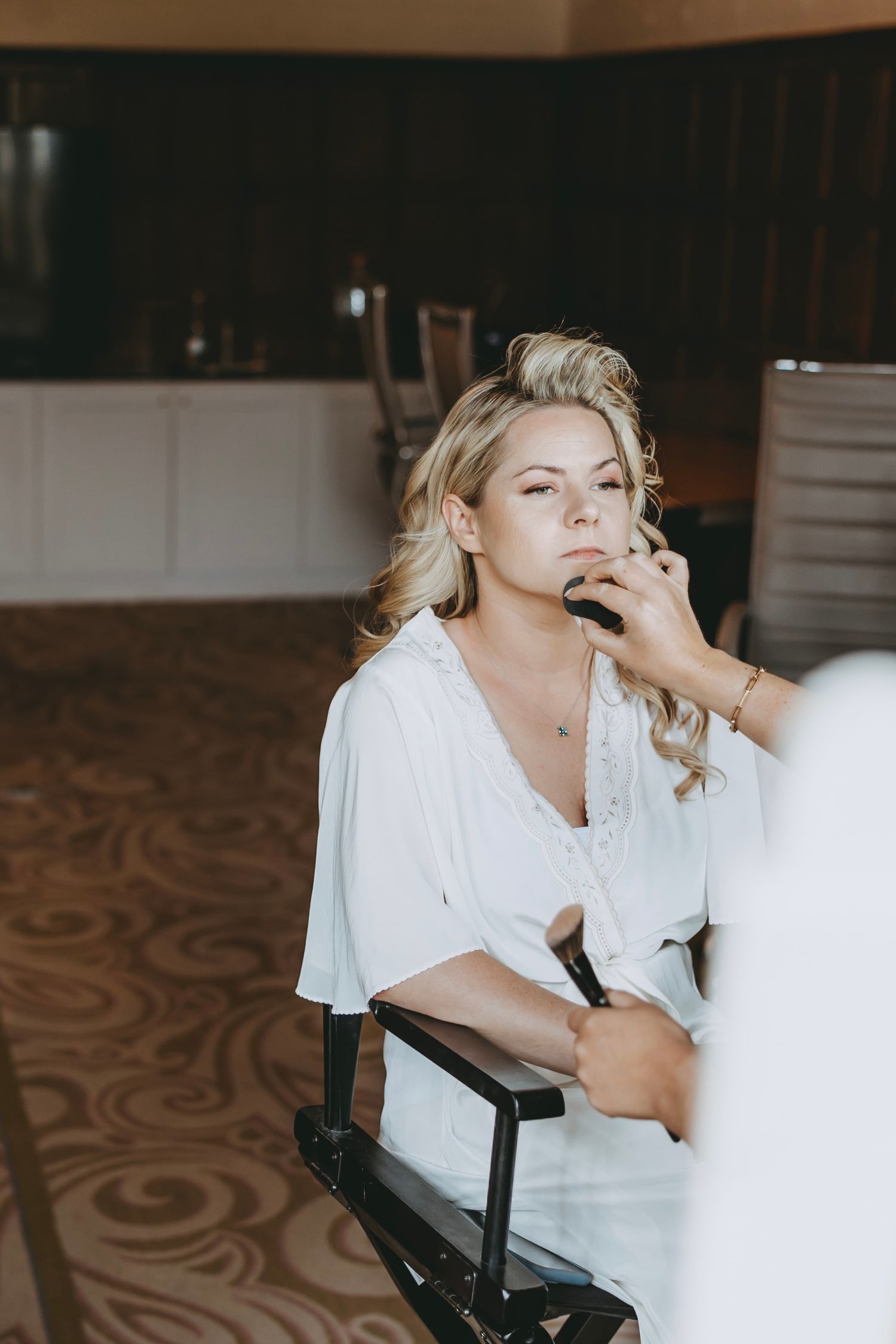 Getting ready scene with professional makeup application in a room with patterned carpet.