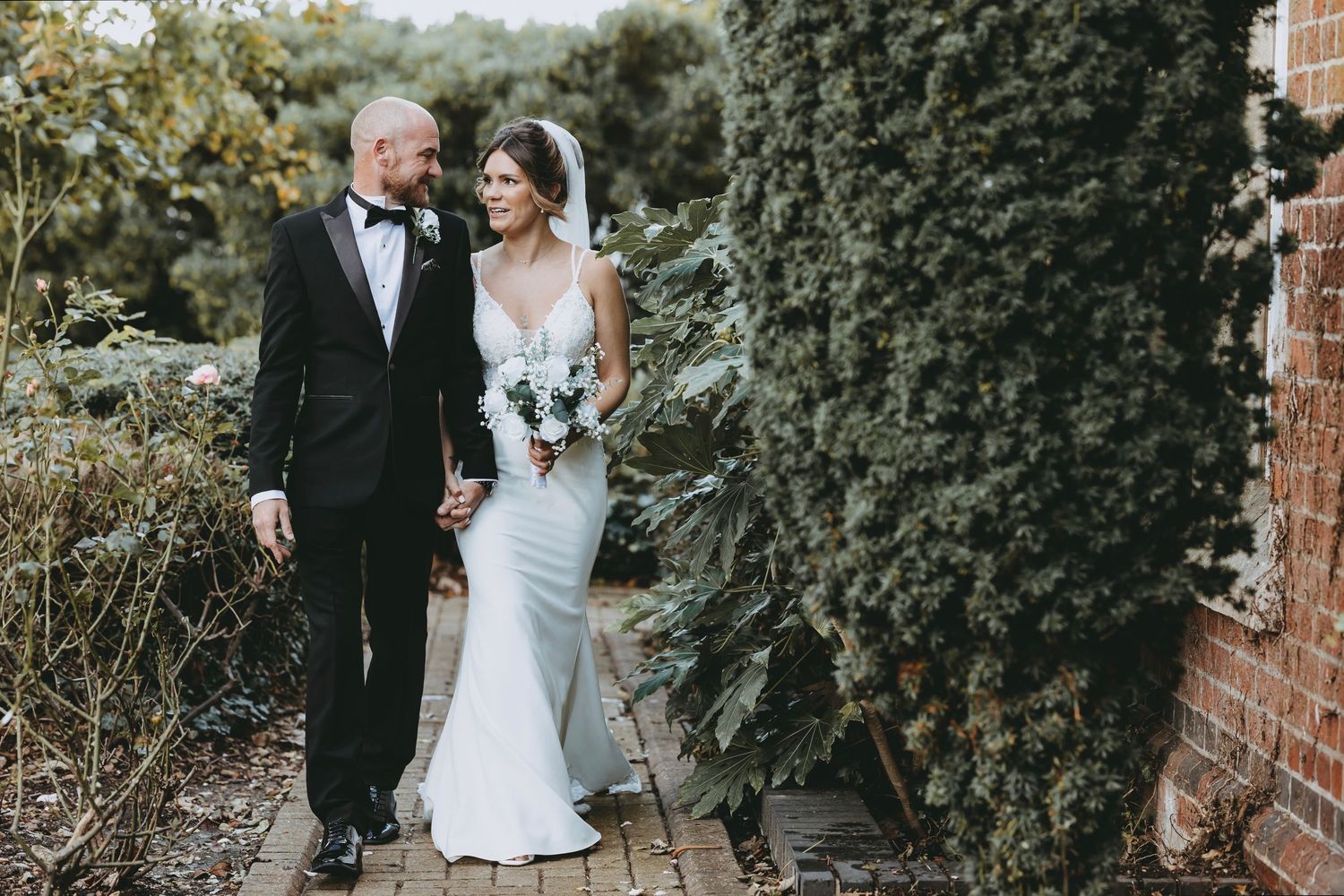 A couple poses in a garden setting with lush green ivy covered walls.