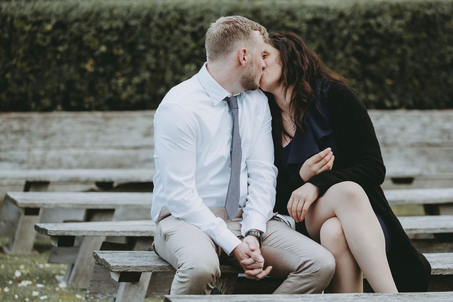 Couple shares an intimate moment on wooden benches at outdoor venue.