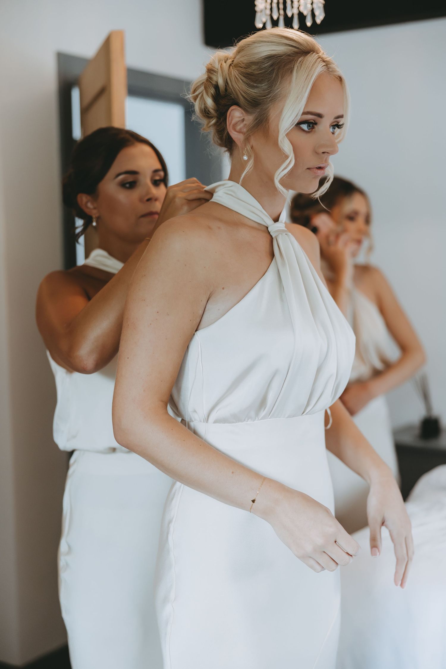 Wedding party members in one-shoulder white dresses assist with final preparations.