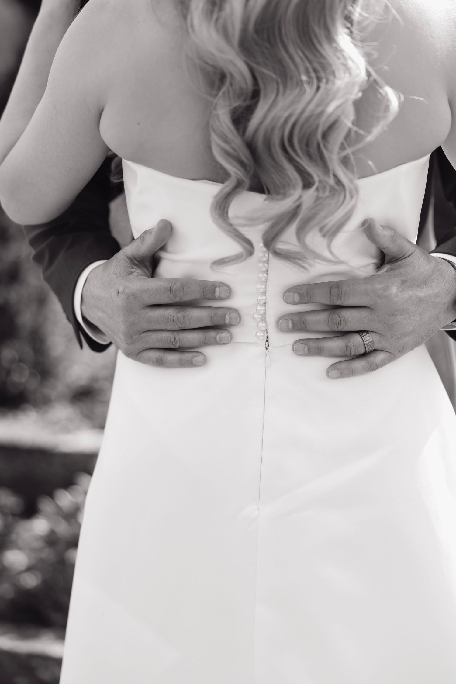 Black and white detail shot of hands on back of wedding dress buttons.
