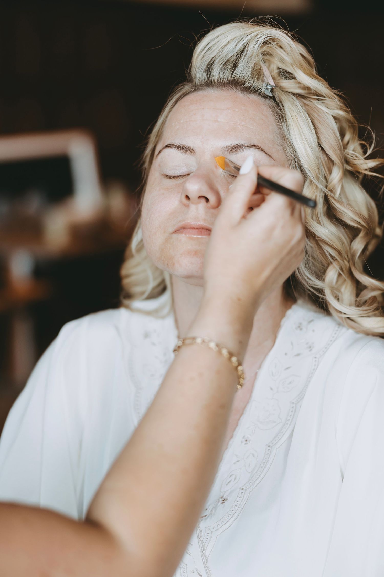 Close-up shots of someone having makeup applied while wearing a white lace dress during bridal preparations.