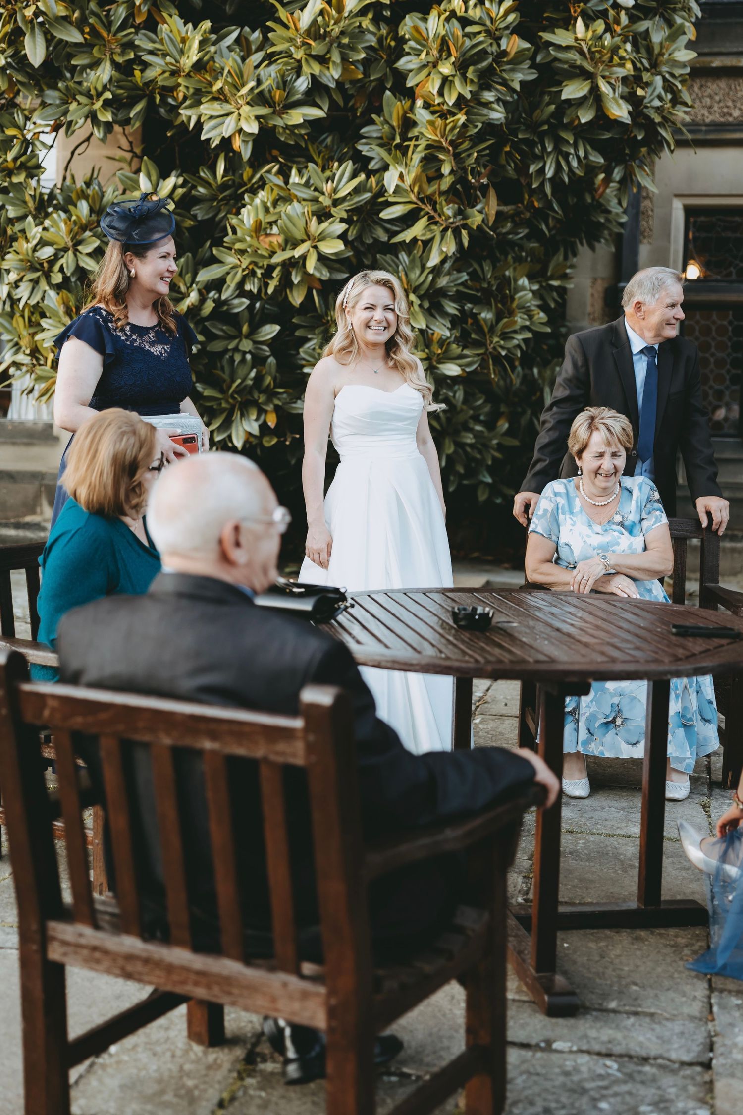 Guests seated at wooden benches under magnolia trees during an outdoor event.