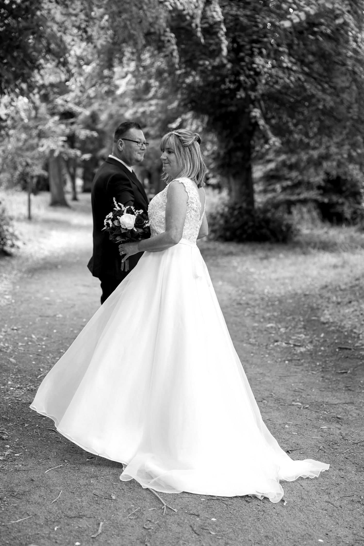 Black and white wedding photo showing a flowing white dress and dark suit in an outdoor garden setting.