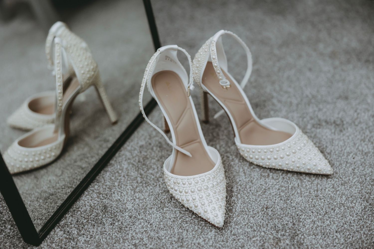 White lace bridal shoes arranged on grey carpet with elegant details.