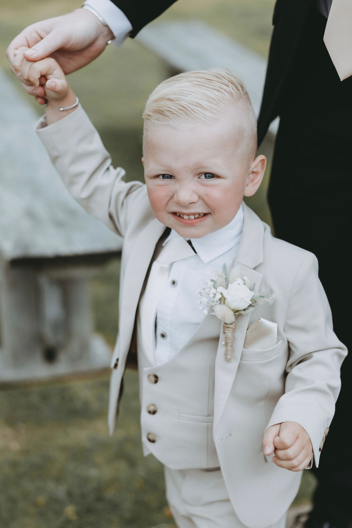 Young ring bearer in white suit smiles while being held during wedding ceremony.