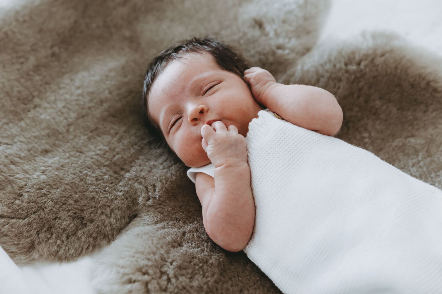 Close-up of tiny newborn baby feet wrapped in soft white blanket against neutral beige background.