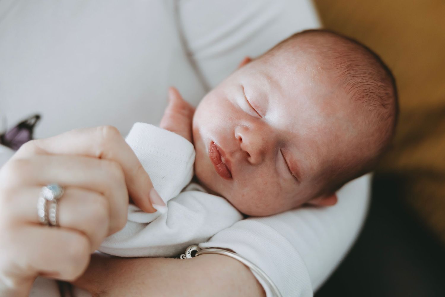Sleeping baby swaddled in white blanket with close up details of tiny hands and peaceful expression.