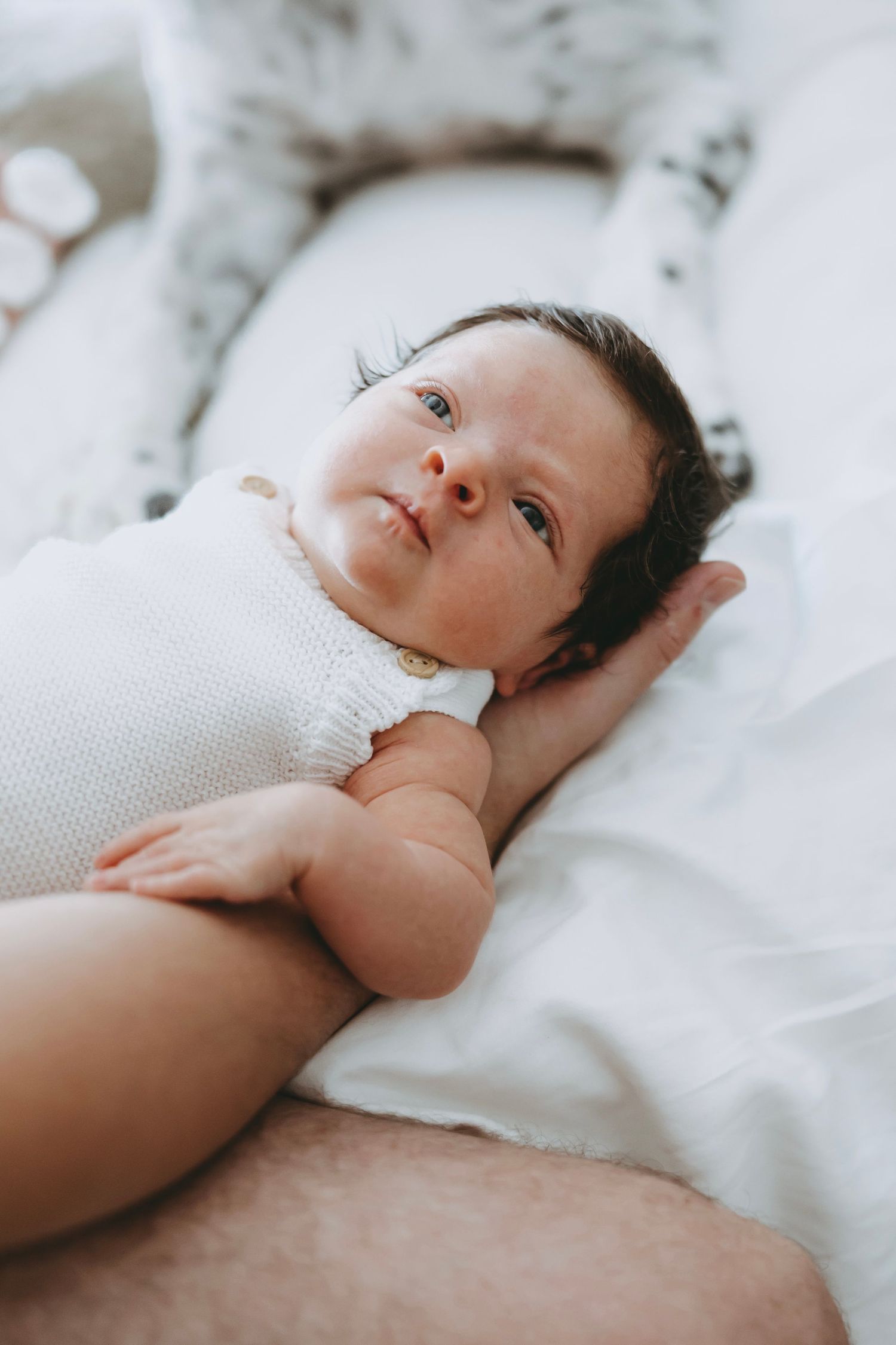 Baby lying on white bedding looking peaceful and content in natural light series of connected photos.