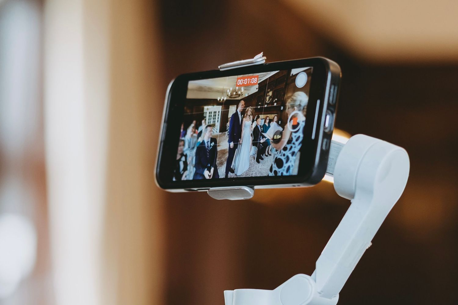 Guest capturing wedding ceremony moments on smartphone in elegant indoor venue.