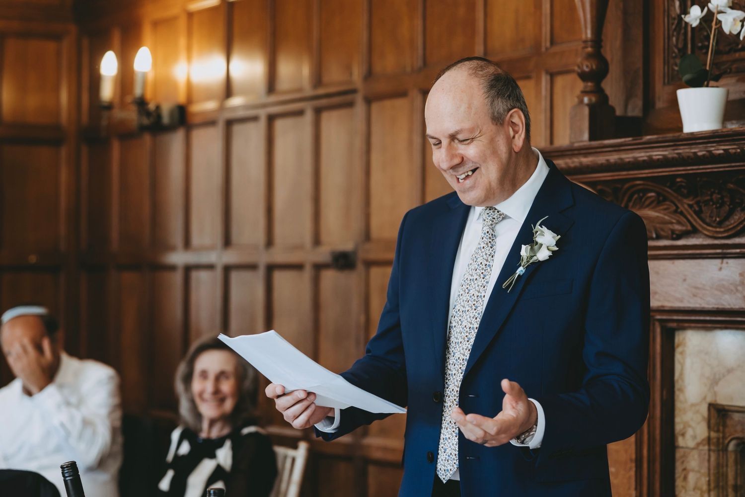 Wedding speaker gestures animatedly during reception speech in elegant venue.