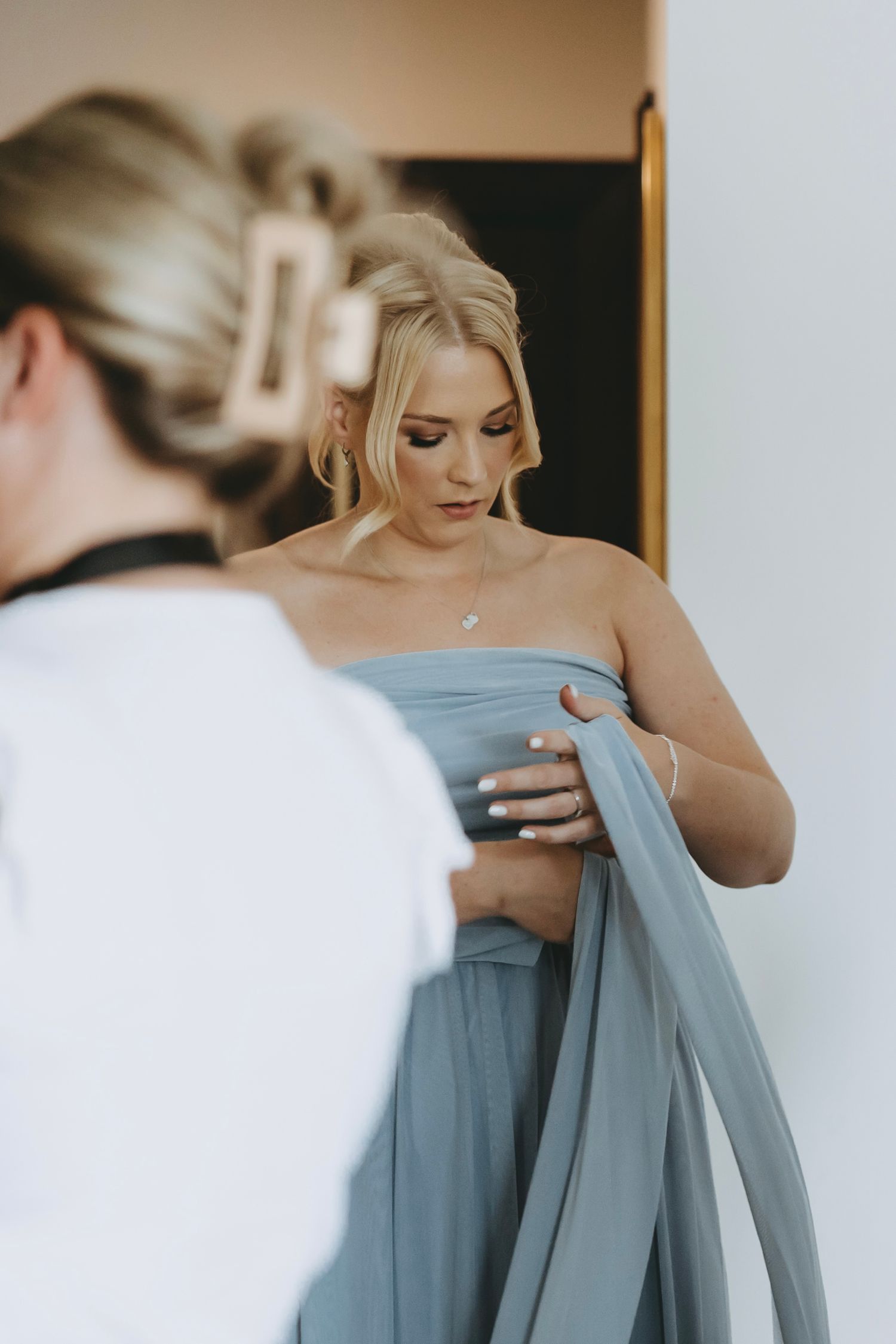 Someone adjusts a dusty blue bridesmaid dress in preparation for a wedding.