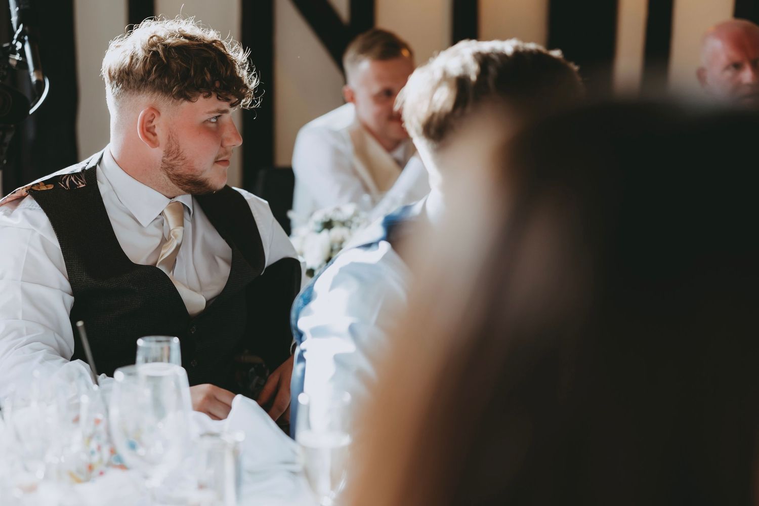 Wedding guests listening intently during reception speeches in timber-framed venue.