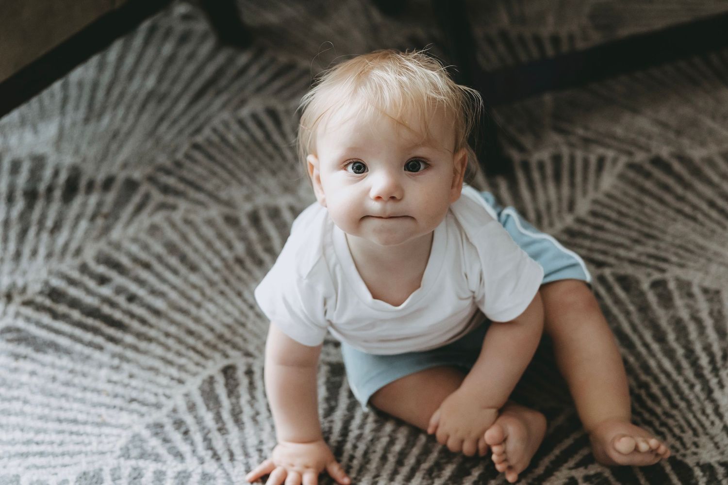 Baby crawling on patterned gray rug in natural light.