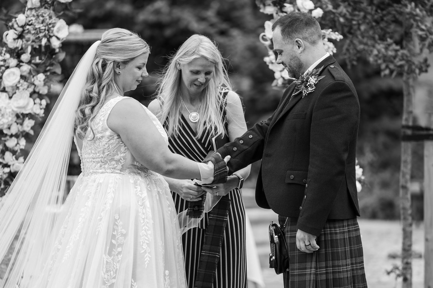 Black and white photo of an intimate outdoor wedding ceremony with guests looking on.