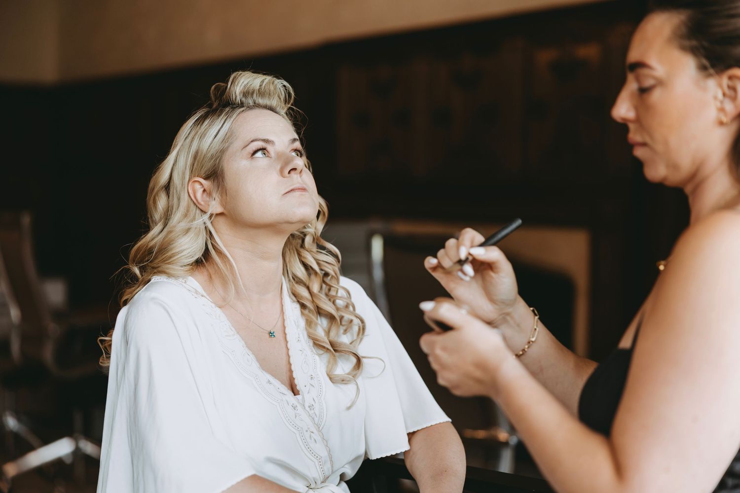 Professional makeup application session with white robe and styled blonde hair.