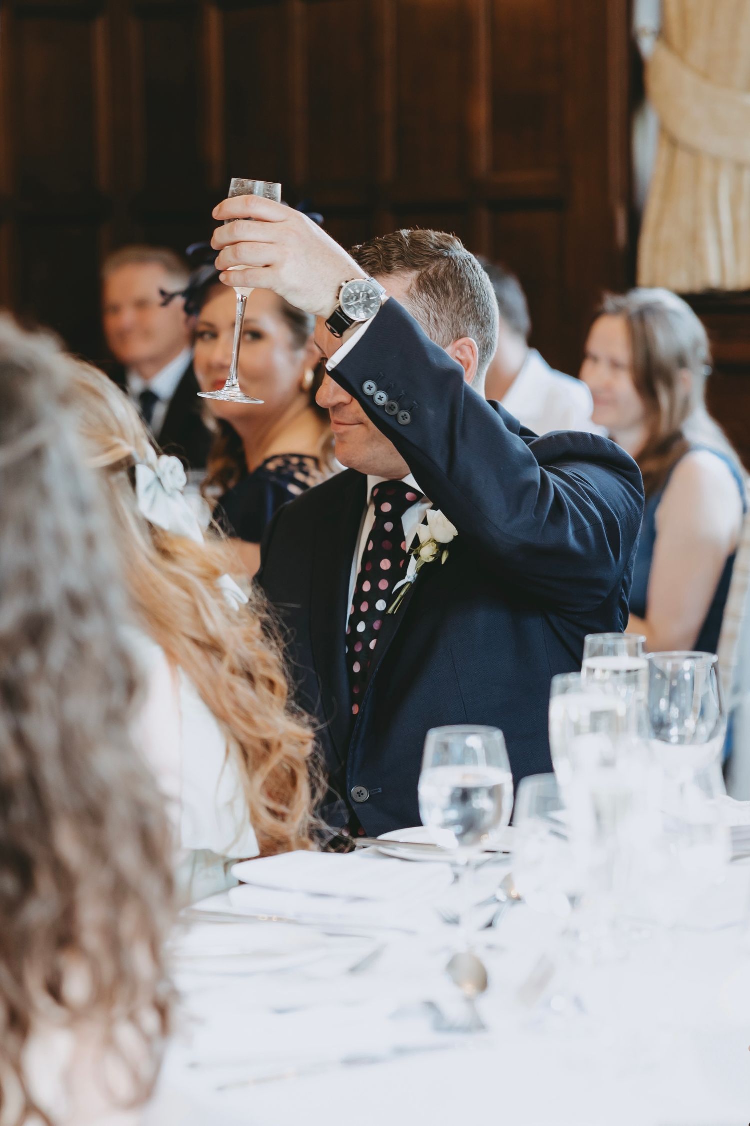 Wedding guests raise glasses during toasts at an elegant reception with formal table settings.