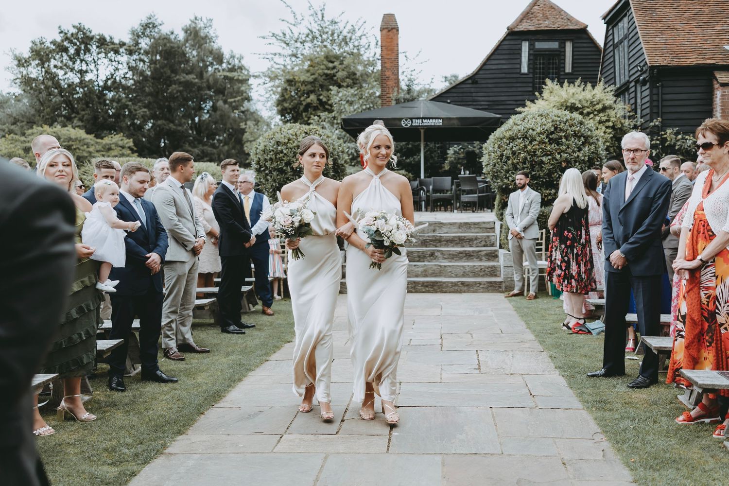 Garden wedding ceremony with guests lined up along a stone path near a historic building.