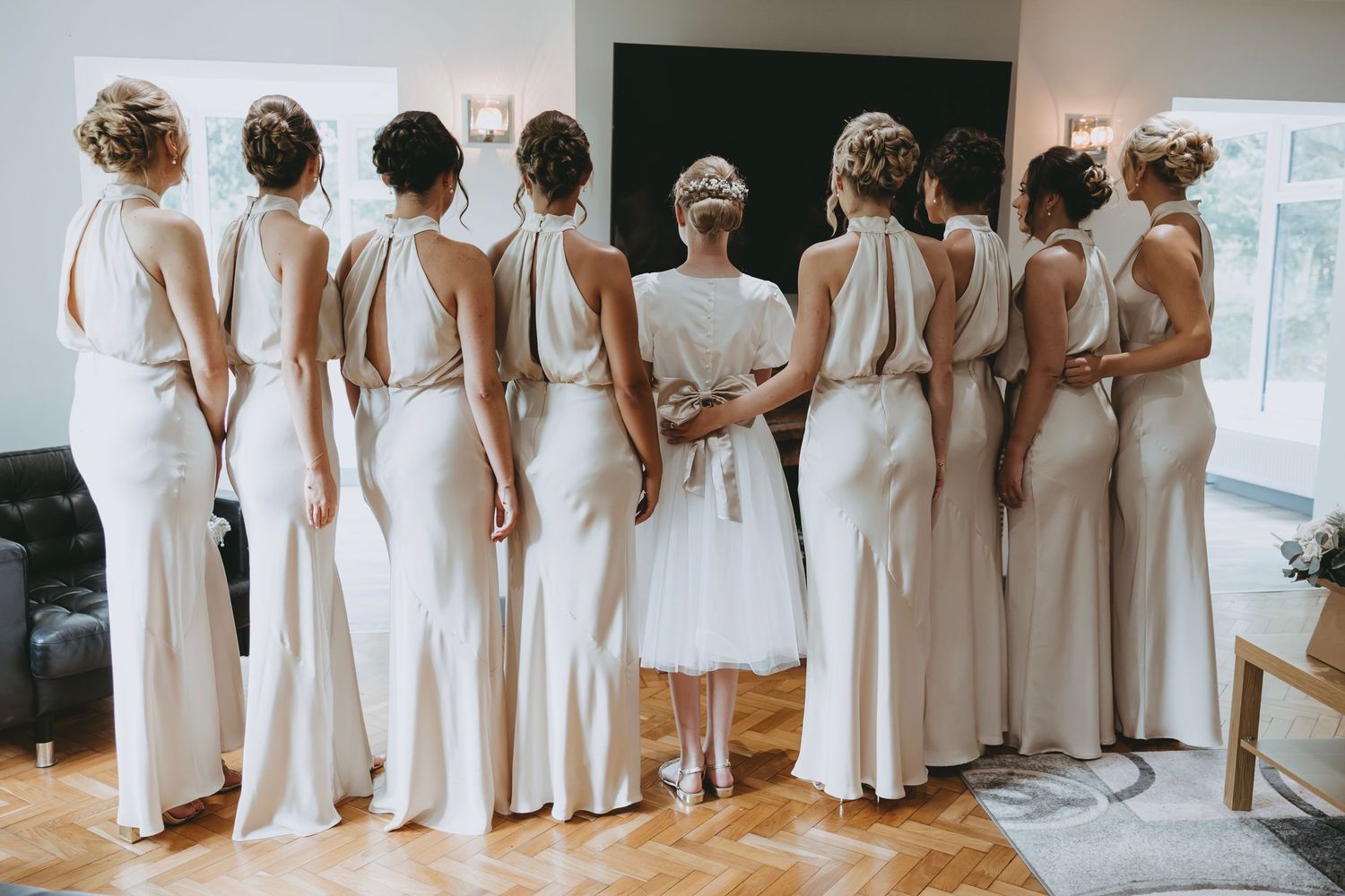 Line of bridesmaids wearing matching white dresses standing together in an indoor venue.