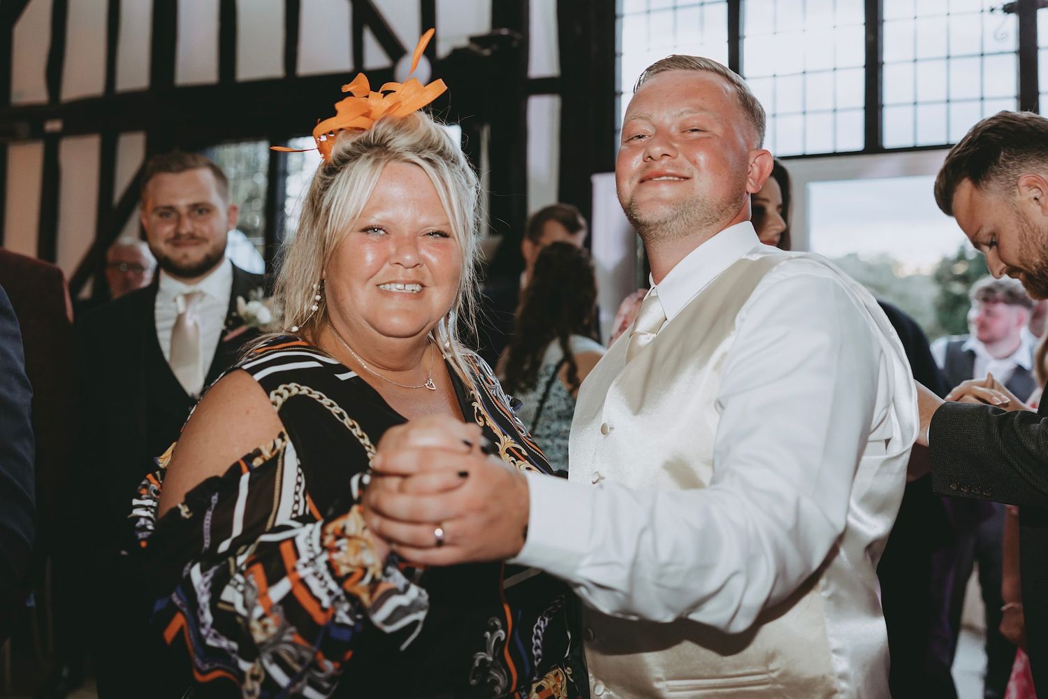 Wedding guests dancing and celebrating at an indoor reception venue with decorative lighting.